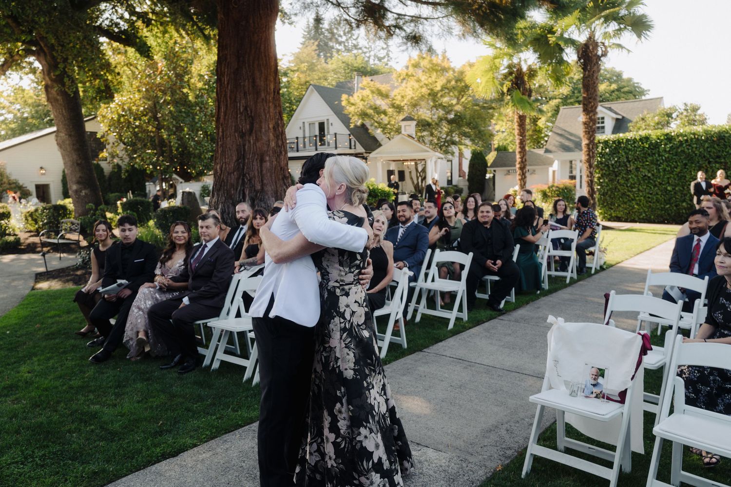 Wedding guests seated in white chairs during an outdoor ceremony.
