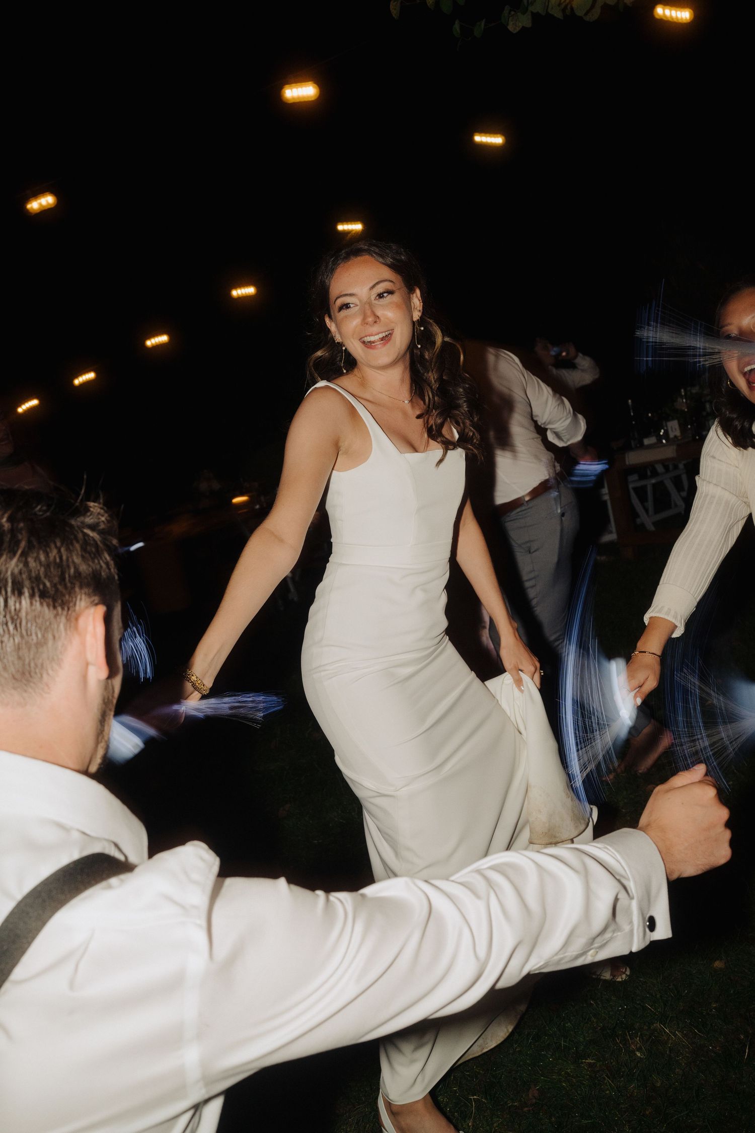 A couple dancing at a nighttime wedding reception with string lights glowing overhead.