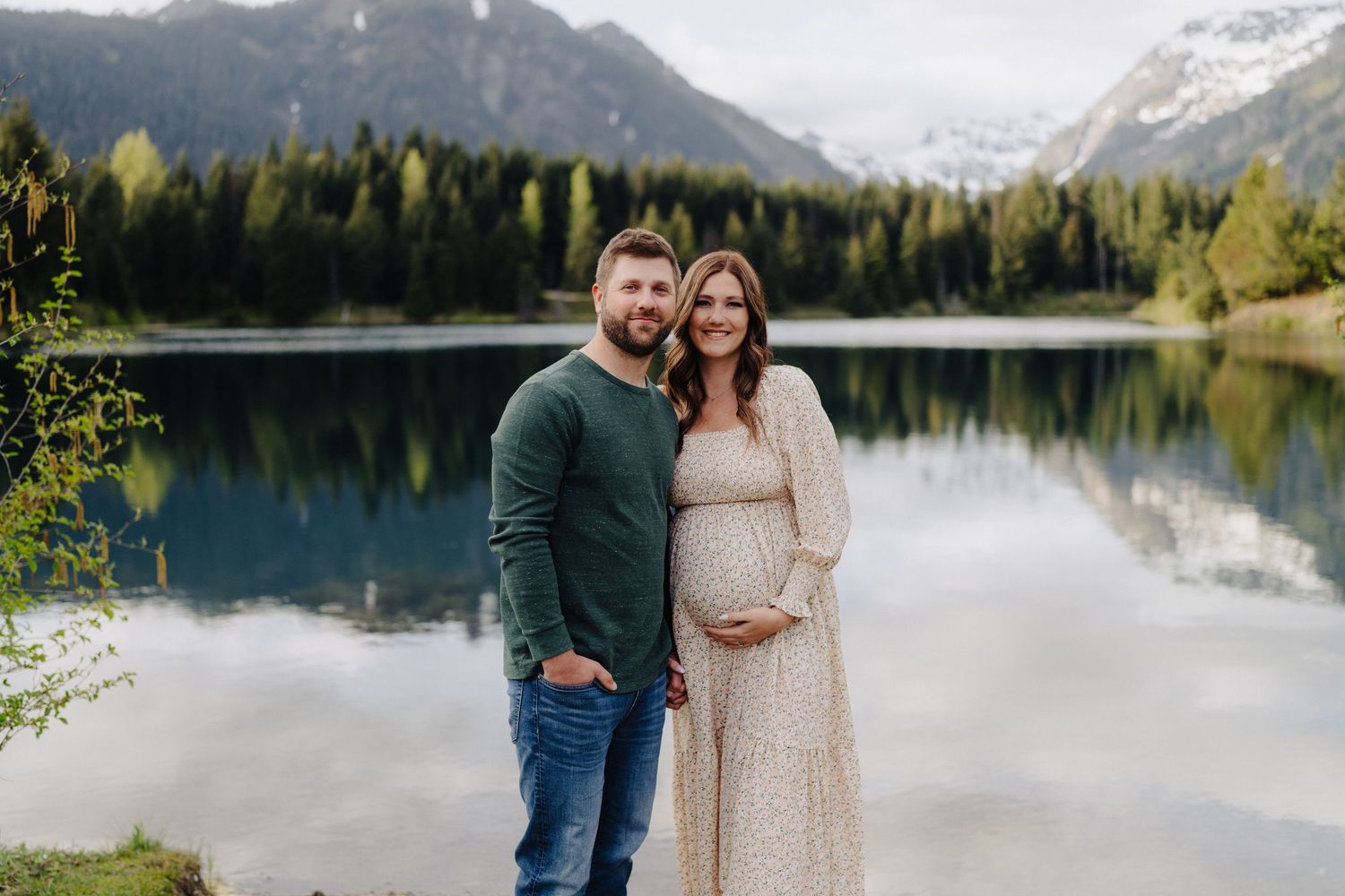 Couple enjoying a serene mountain lake view with snow-capped peaks and evergreen forests in the background.