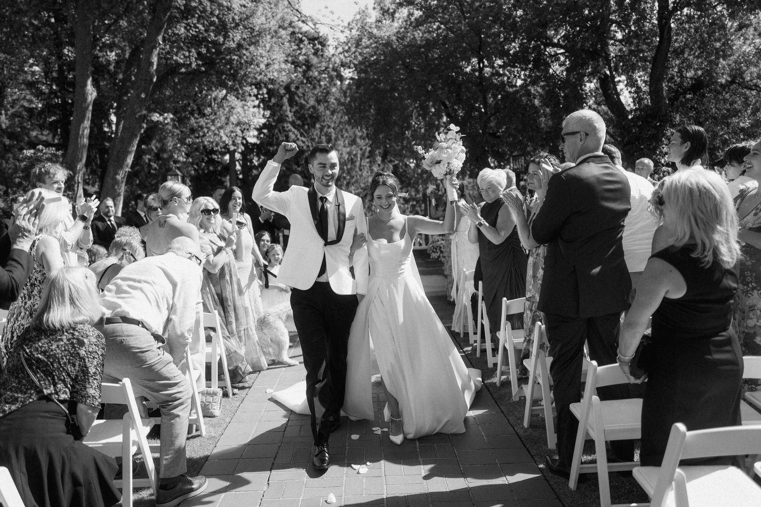 Wedding guests gather outdoors in a garden setting for a celebratory reception on a sunny afternoon.