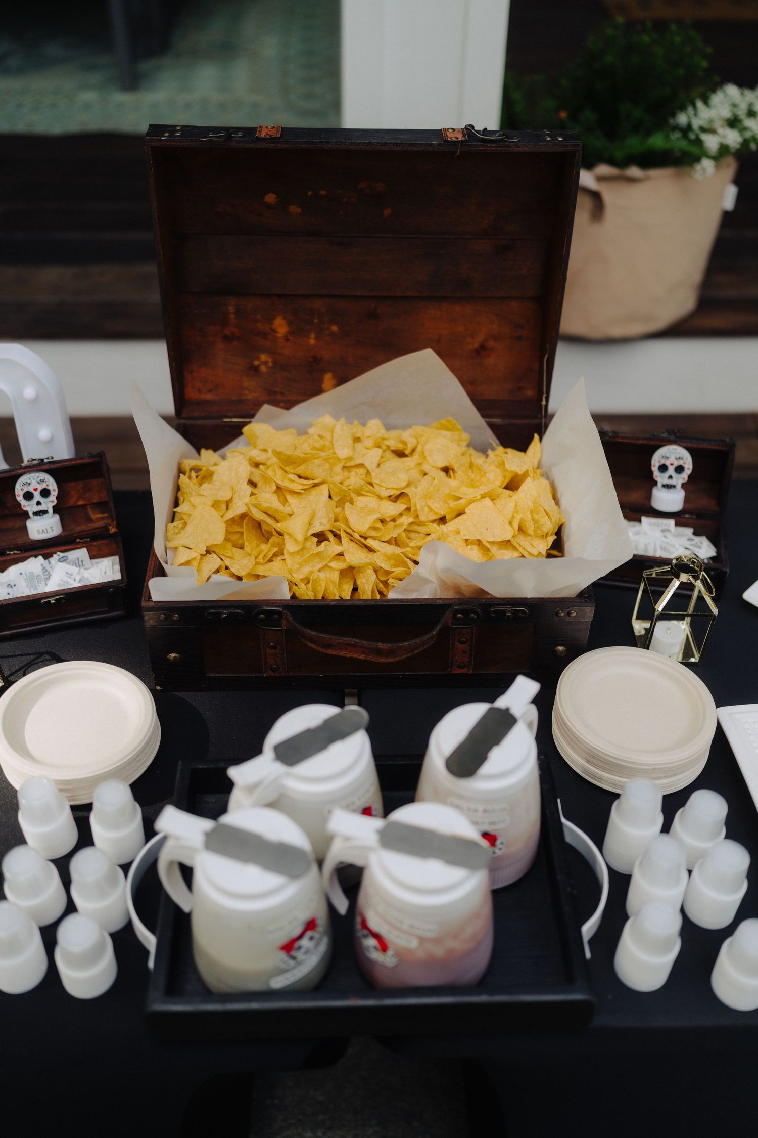 A rustic wooden chest filled with tortilla chips and surrounded by white serving containers.