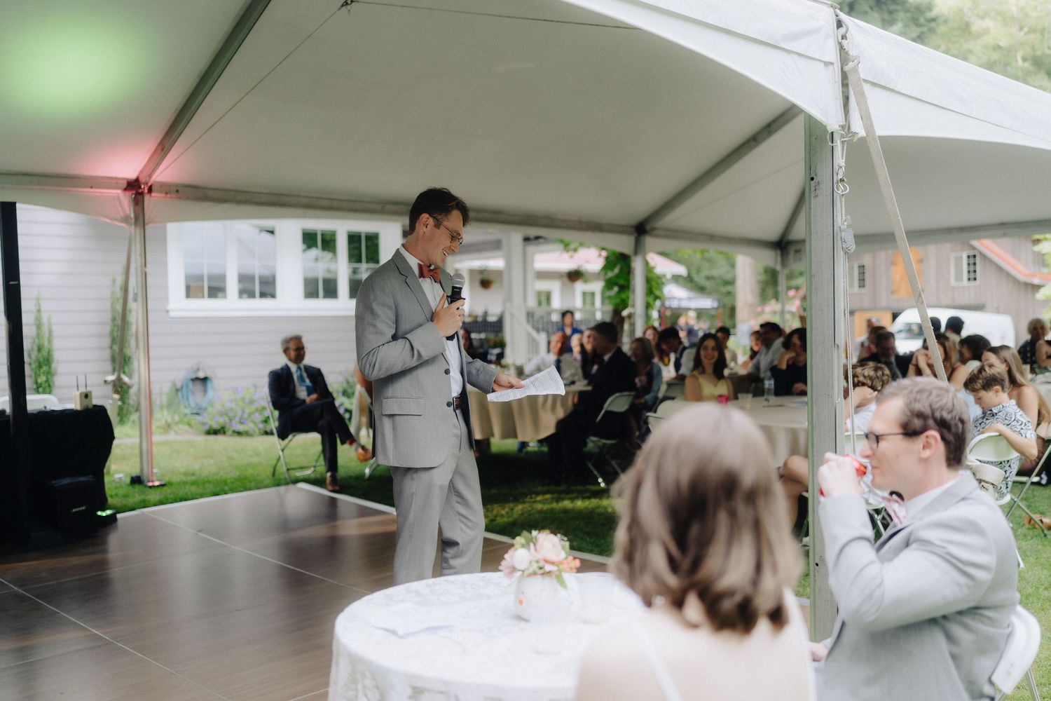 Wedding speech being delivered under white tent during outdoor reception.