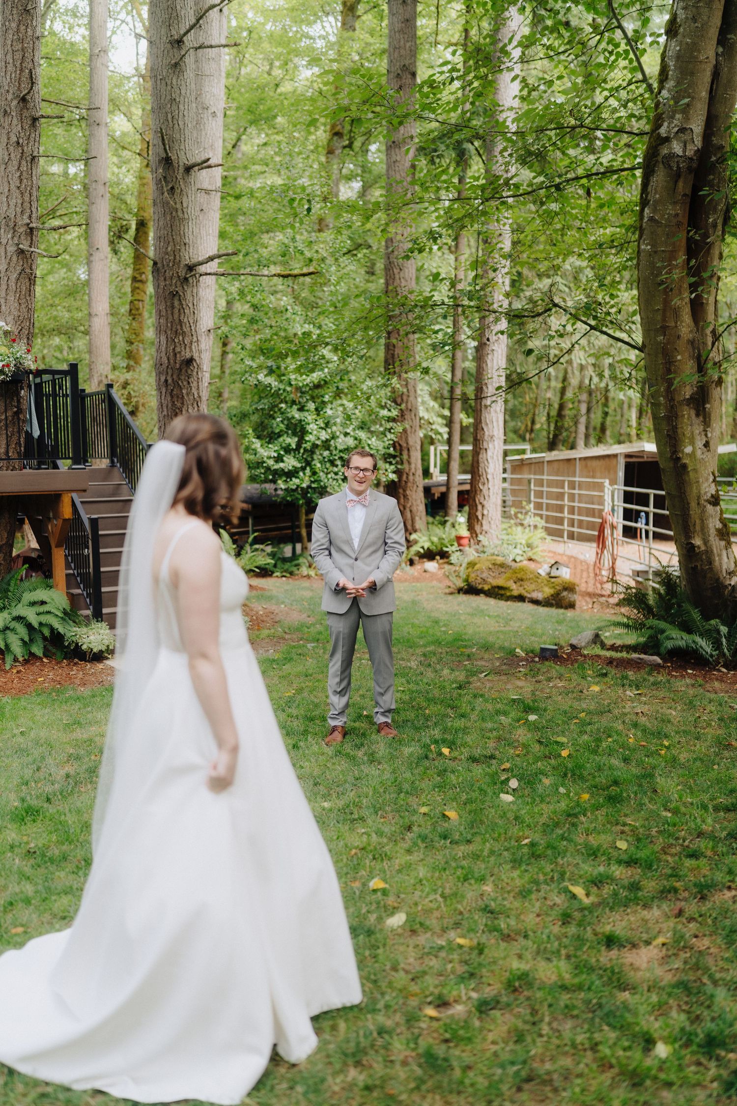 A wedding first look moment unfolds in a serene wooded setting with tall trees and natural light.