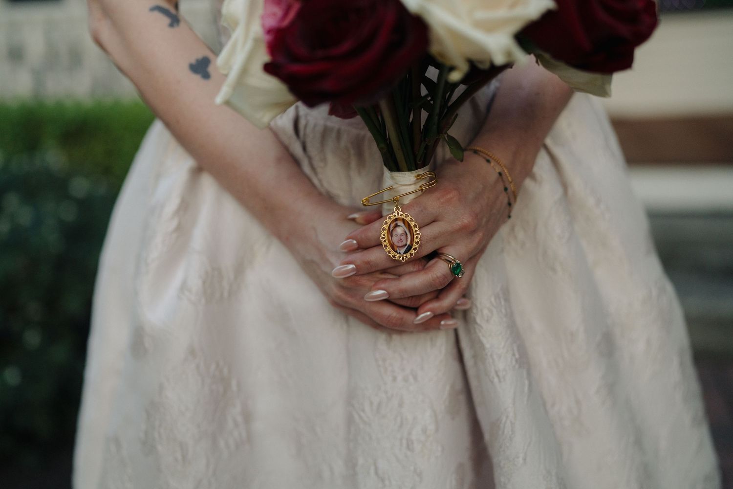 Close-up of hands holding a burgundy rose bouquet, showcasing an ornate ring and white dress details.