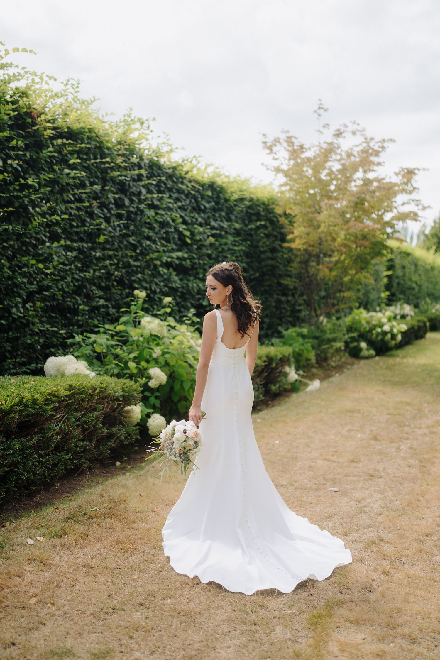 A flowing white wedding dress twirls gracefully against a garden backdrop with green hedges.