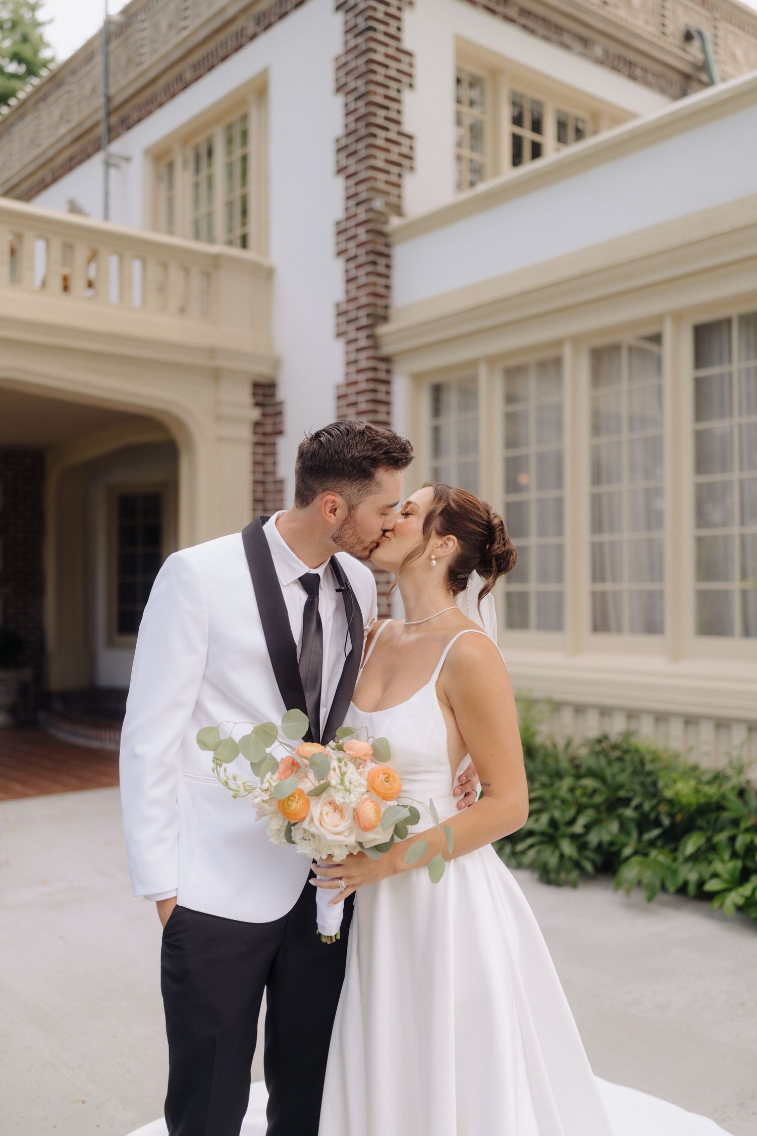 Elegant wedding couple shares romantic moments outside a grand white colonial building.