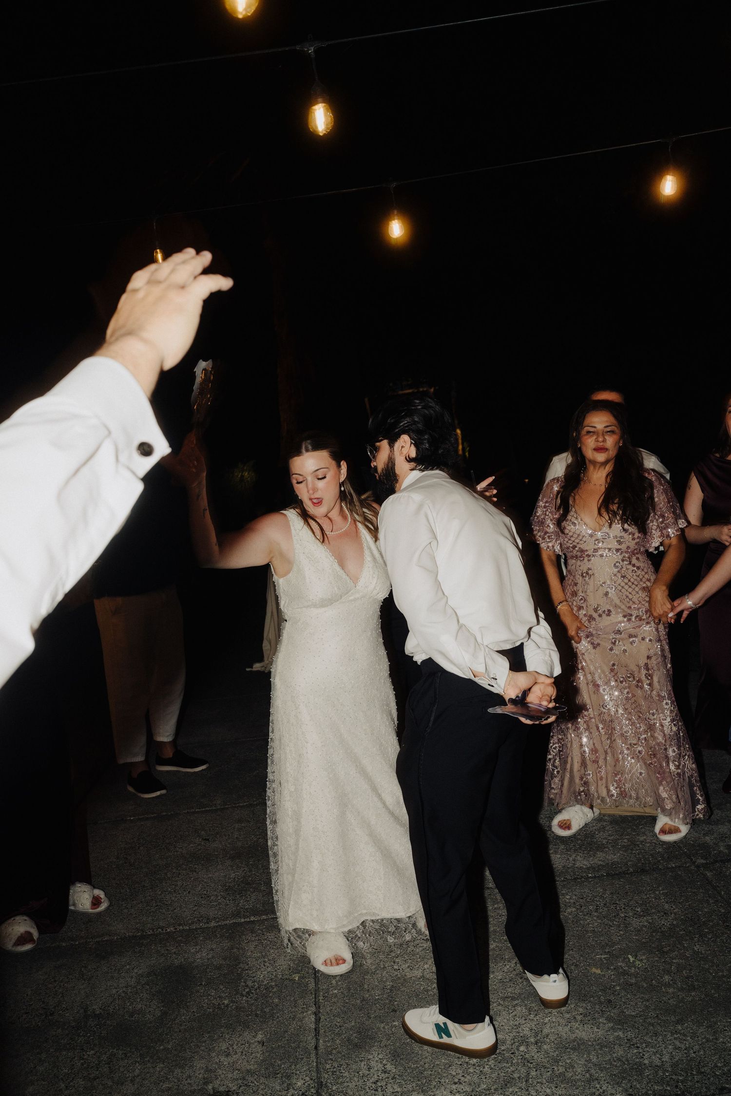 Wedding party dancing and celebrating on a dark dance floor with ambient lighting.