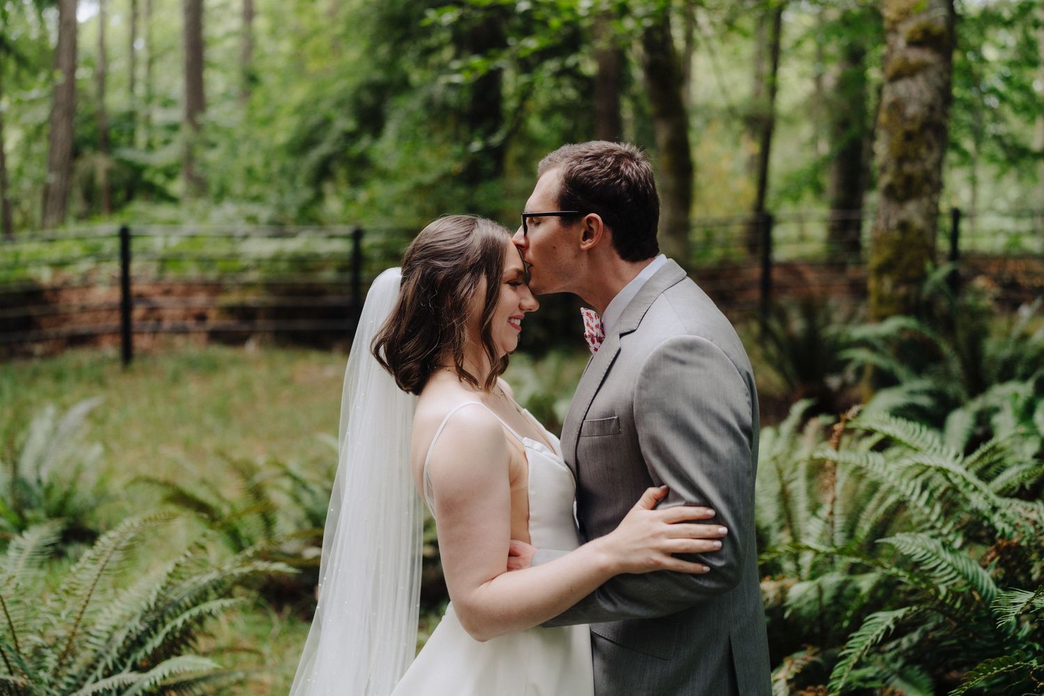 Intimate wedding moment captured in a lush forest setting with ferns and greenery.
