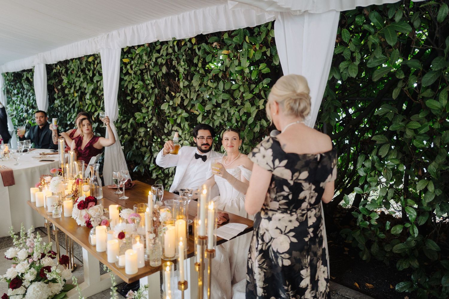 Elegant wedding reception table settings with candlelight and greenery under a white tent.