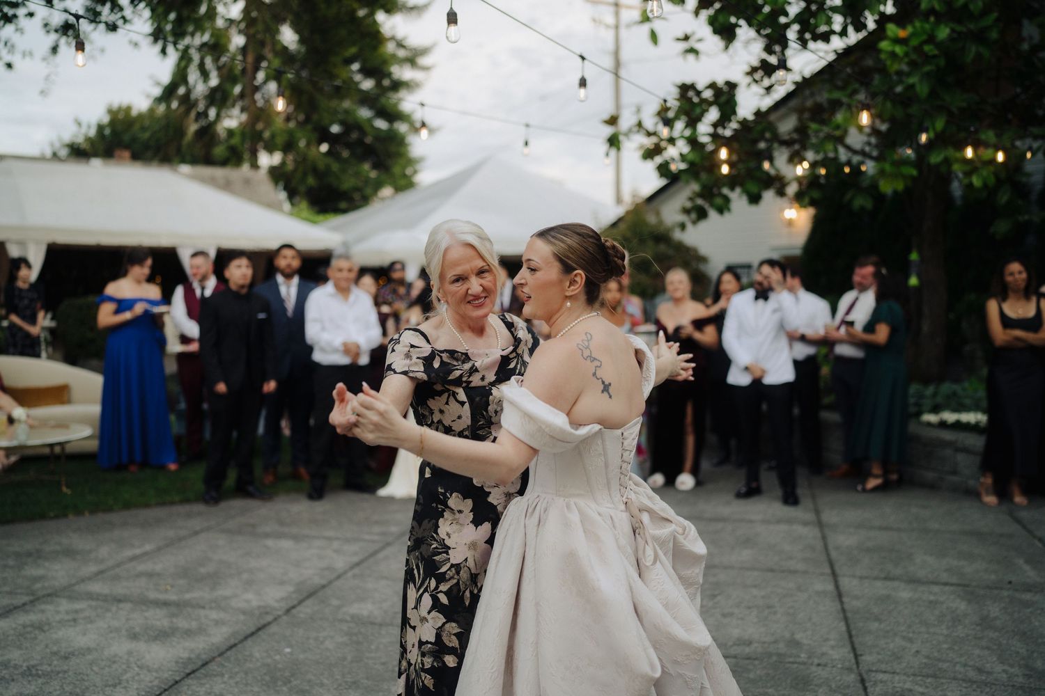 Touching moment during wedding dance as guests look on at outdoor evening reception.