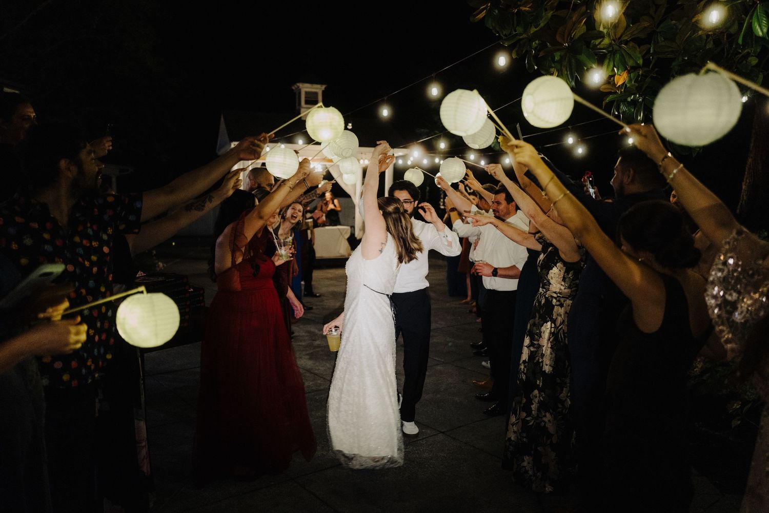 Wedding celebration at night with glowing paper lanterns and guests raising their arms in celebration.