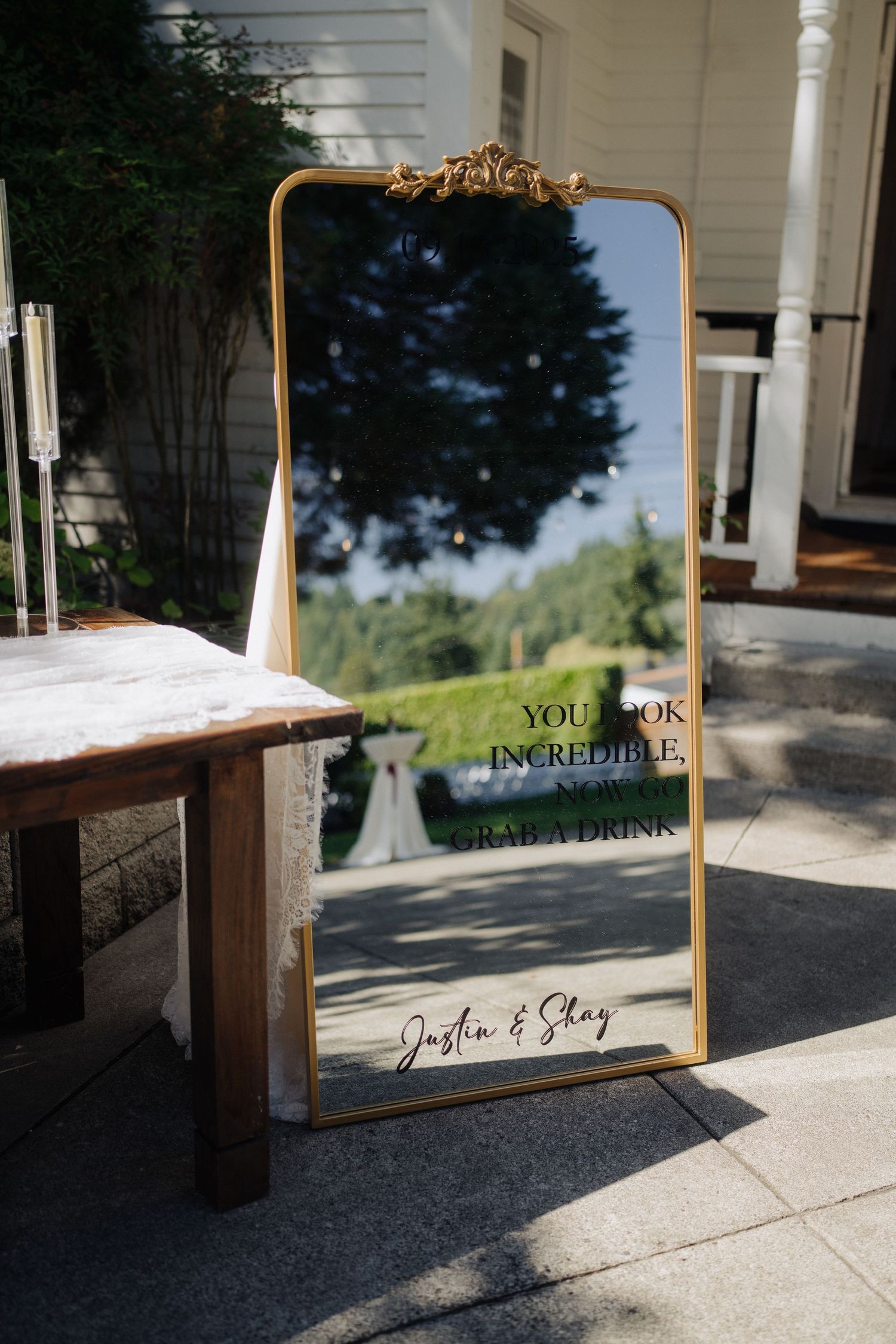 Framed wedding sign with gold accents sits on rustic wooden table at outdoor venue.