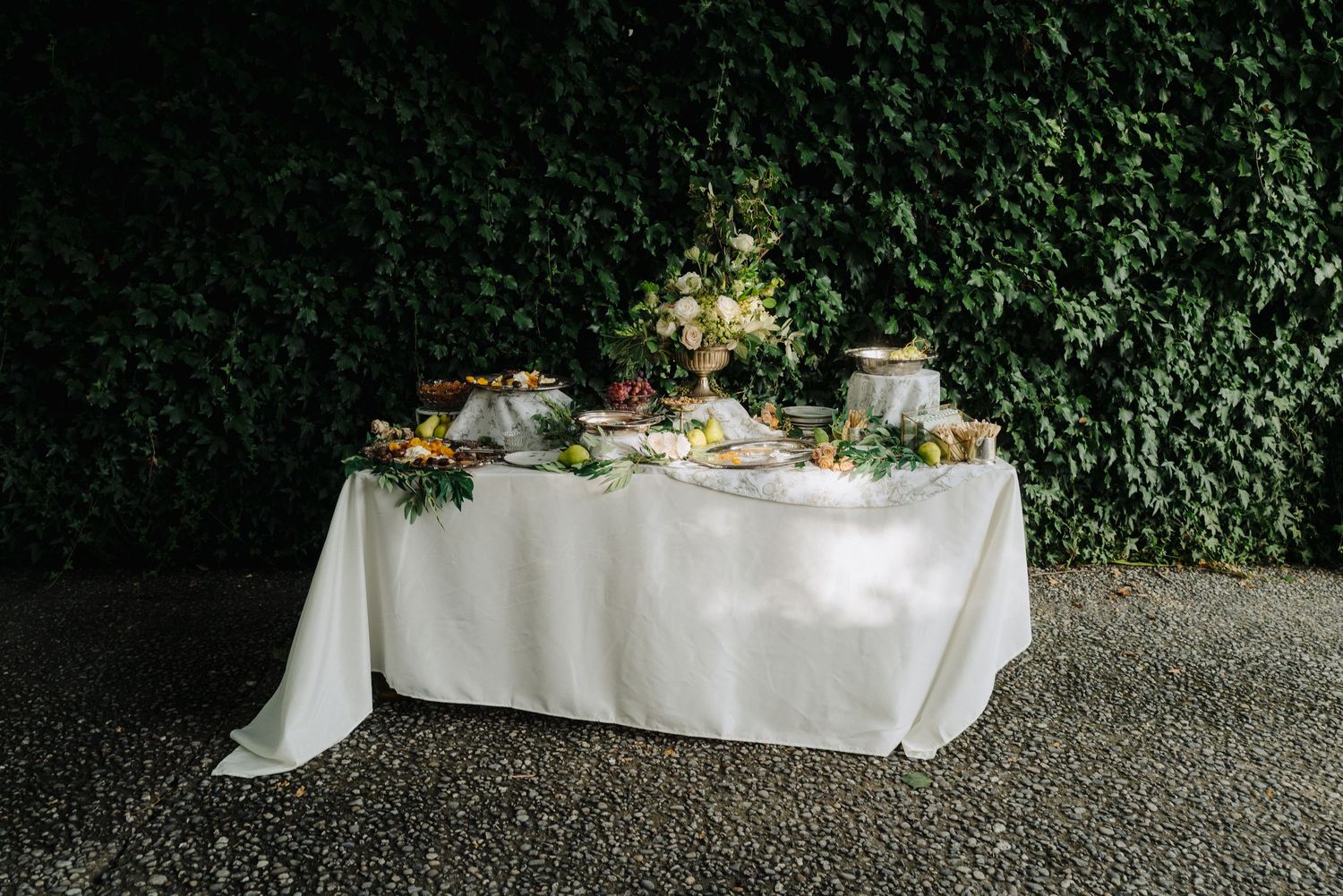 An elegant wedding reception table setup with white linens and greenery against an ivy wall.