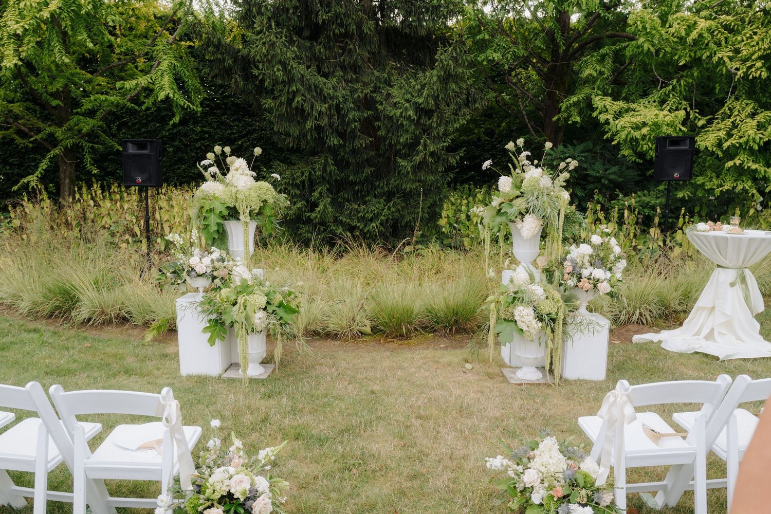 Elegant outdoor wedding venue with white chairs and floral decorations arranged on a grassy lawn.
