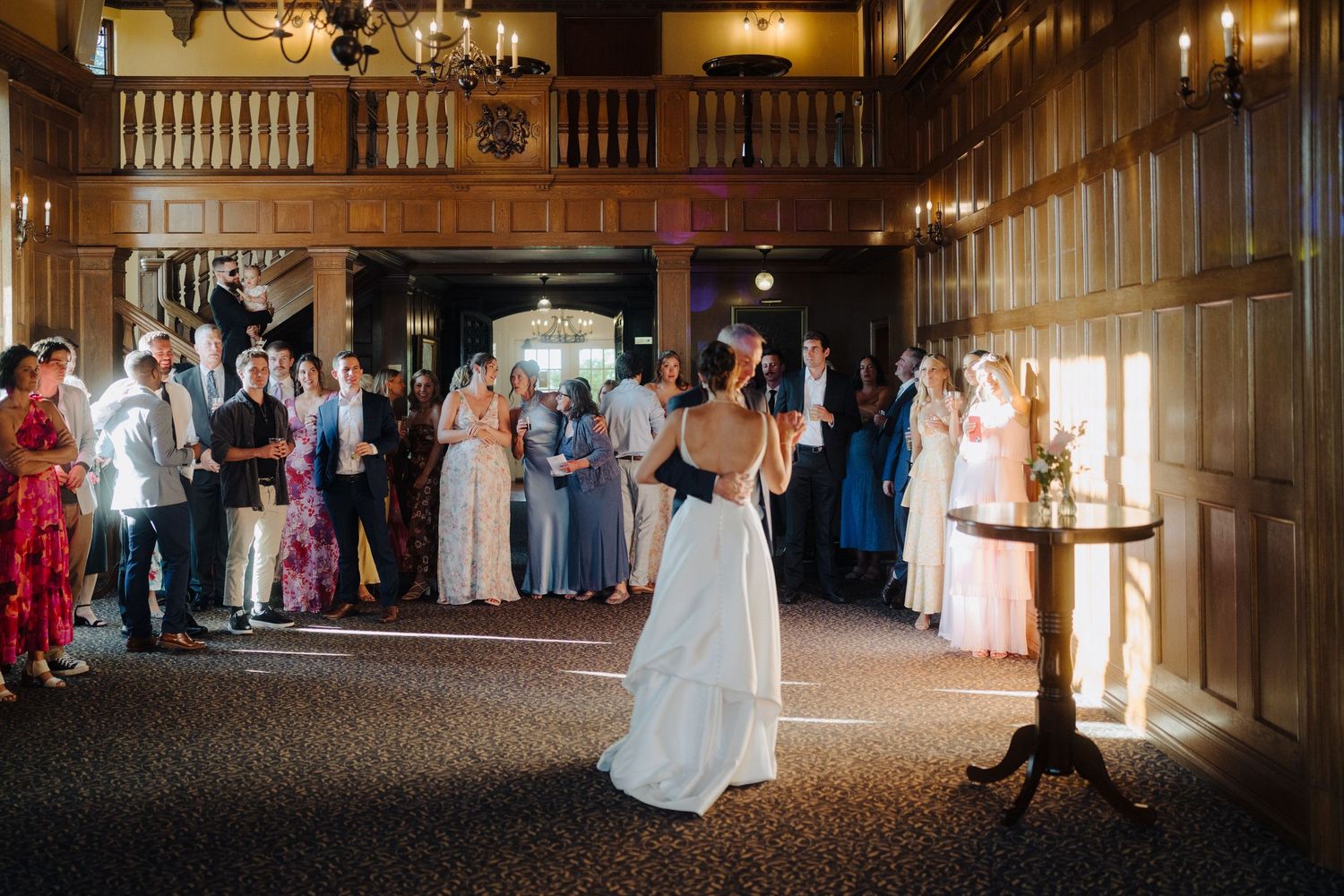 Wedding guests gather to watch a dance performance in an elegant wooden-paneled venue.