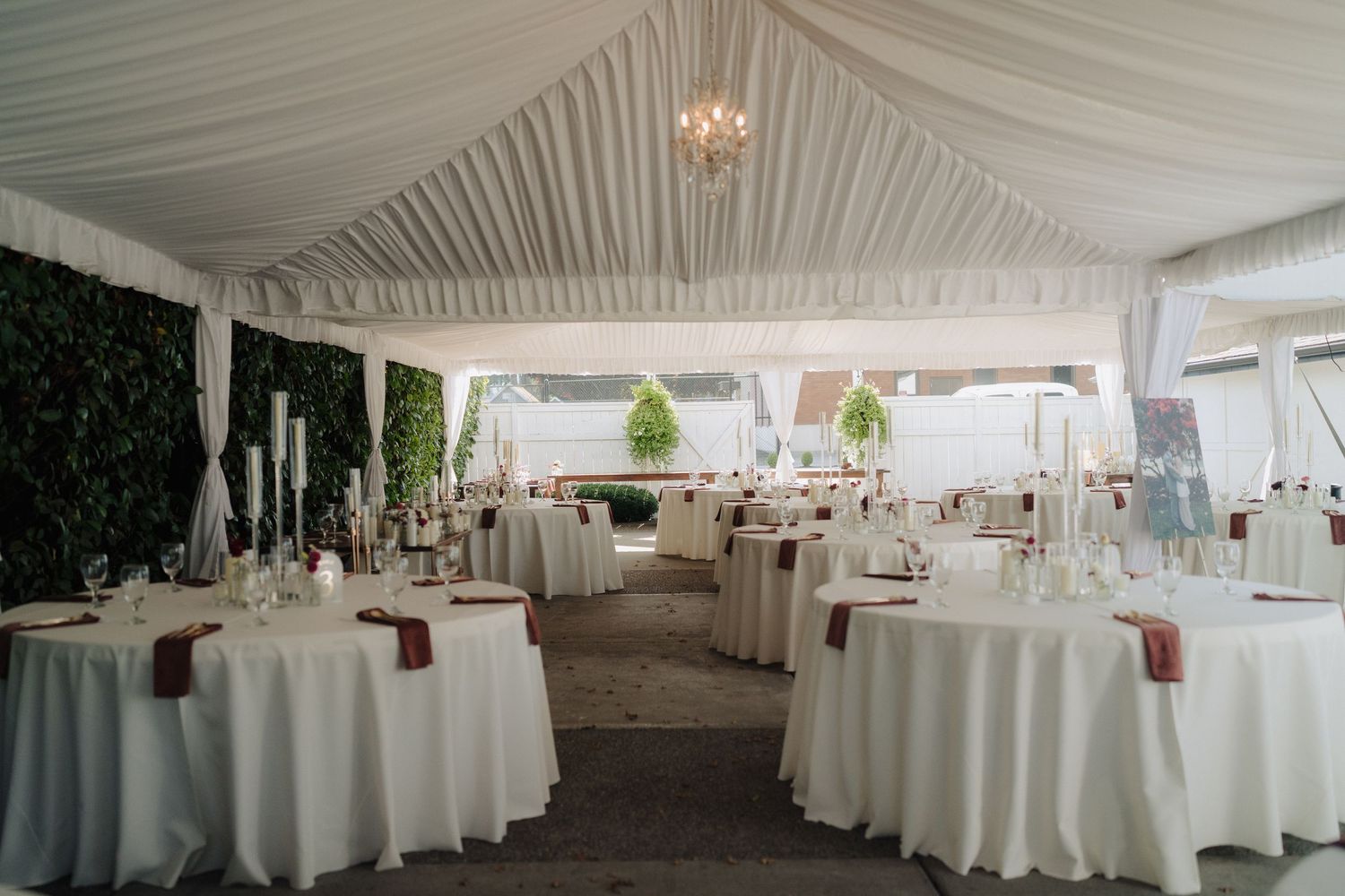 Elegant white tent reception setup with round tables, white linens, and chandelier lighting.