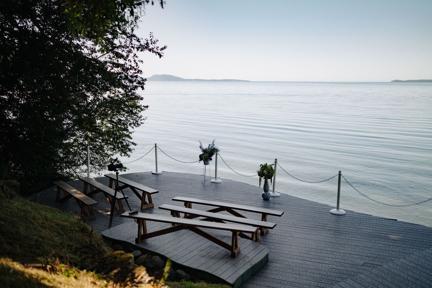 Wooden benches arranged on a waterfront deck with scenic ocean views for an outdoor ceremony.