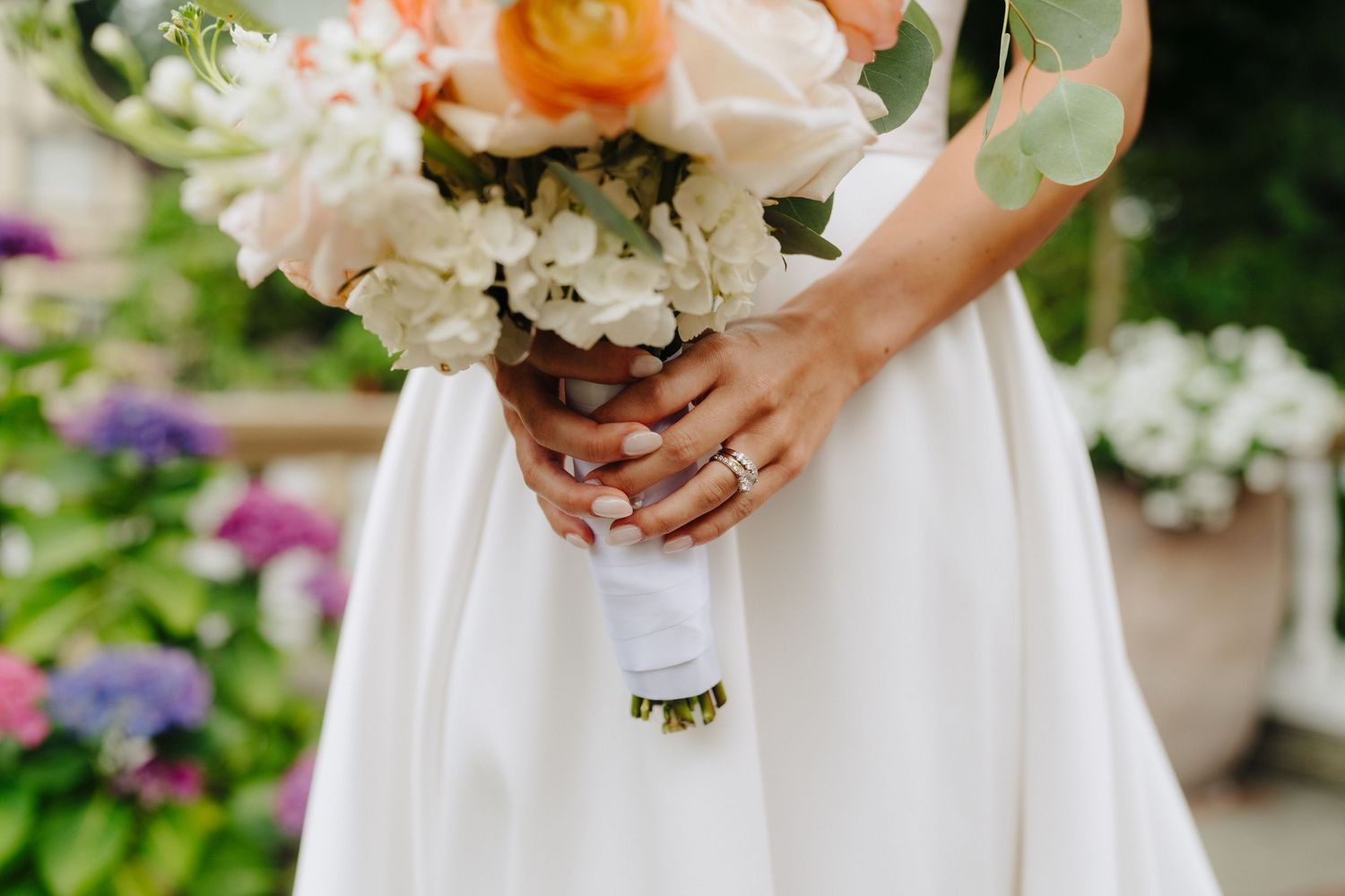 Close-up of delicate white and pink floral wedding bouquets held against white dresses.