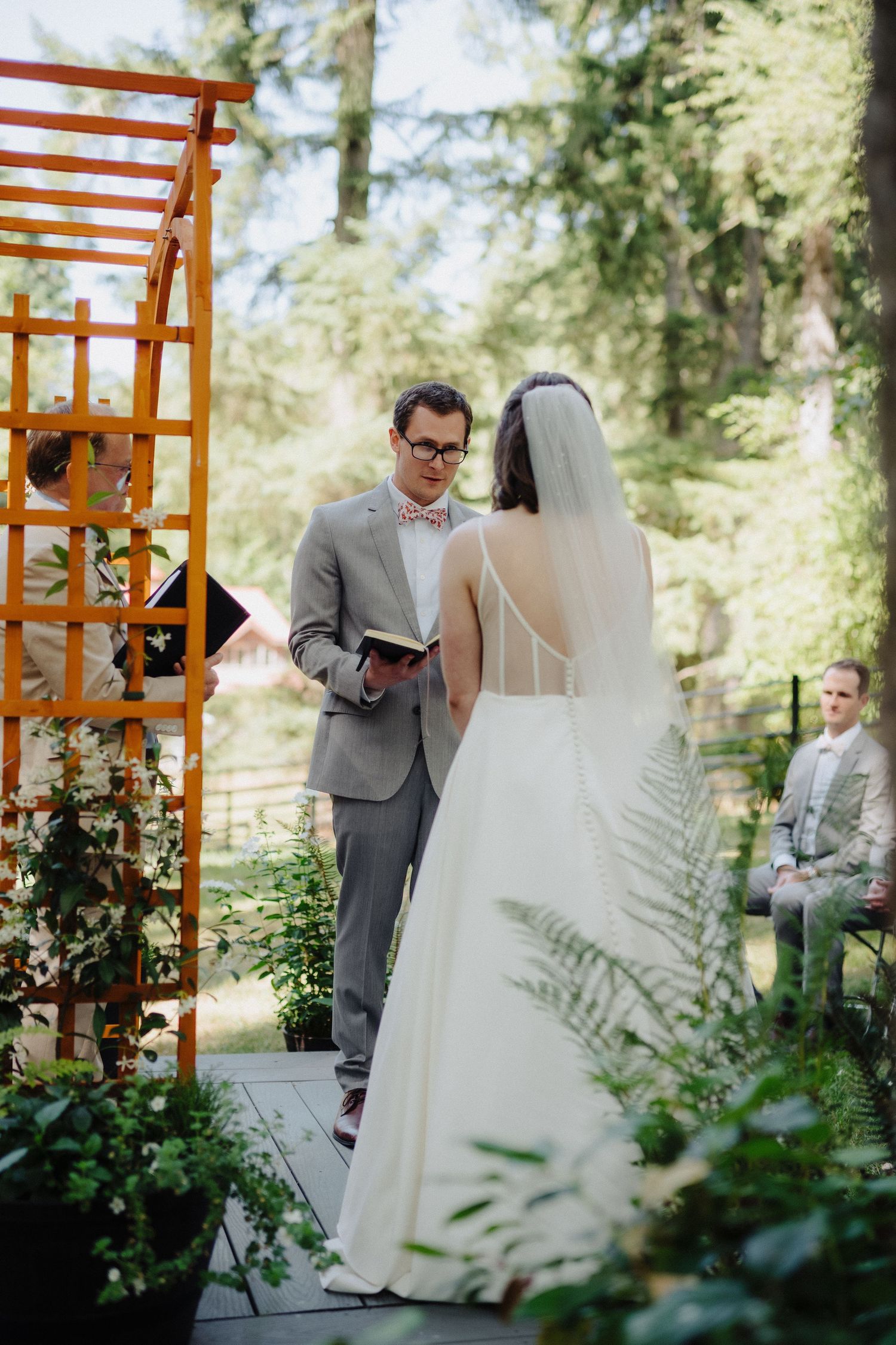Romantic first look moment between newlyweds under a wooden arbor surrounded by greenery and ferns.