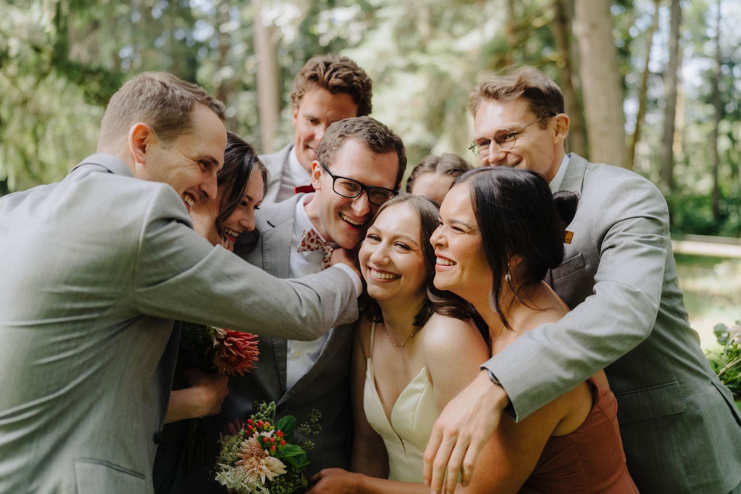 Wedding party shares an intimate group moment outdoors while laughing together.