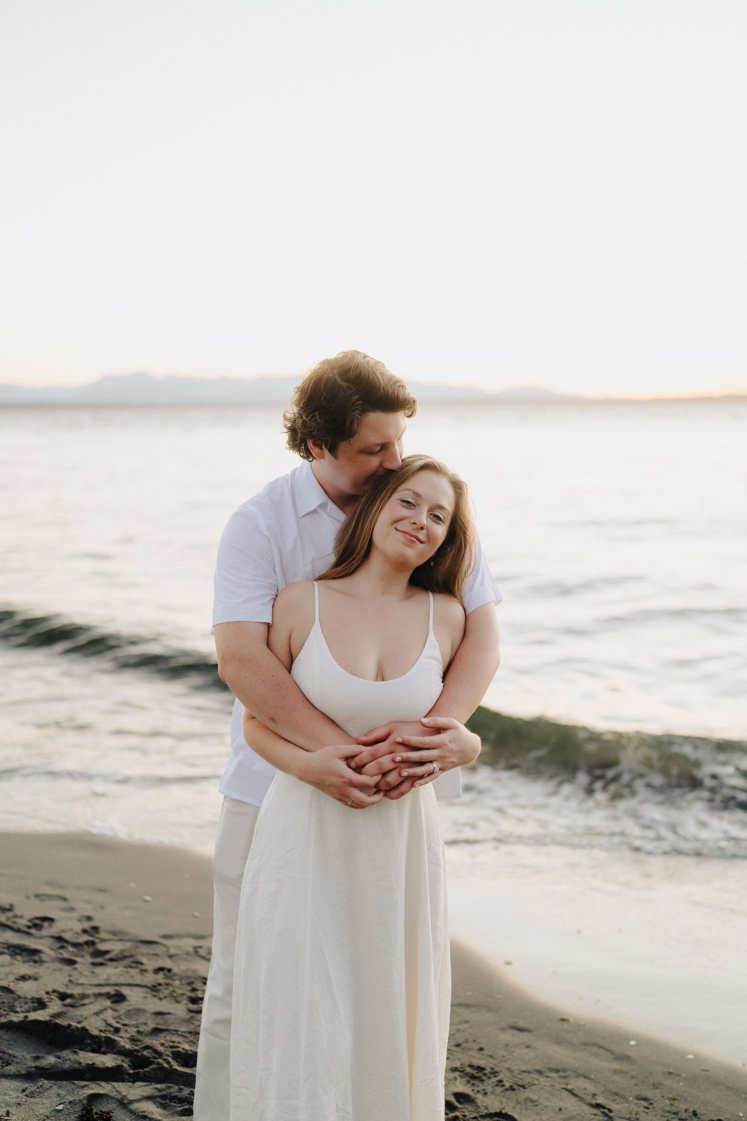 A tender beachside embrace between a couple in white clothing at sunset.