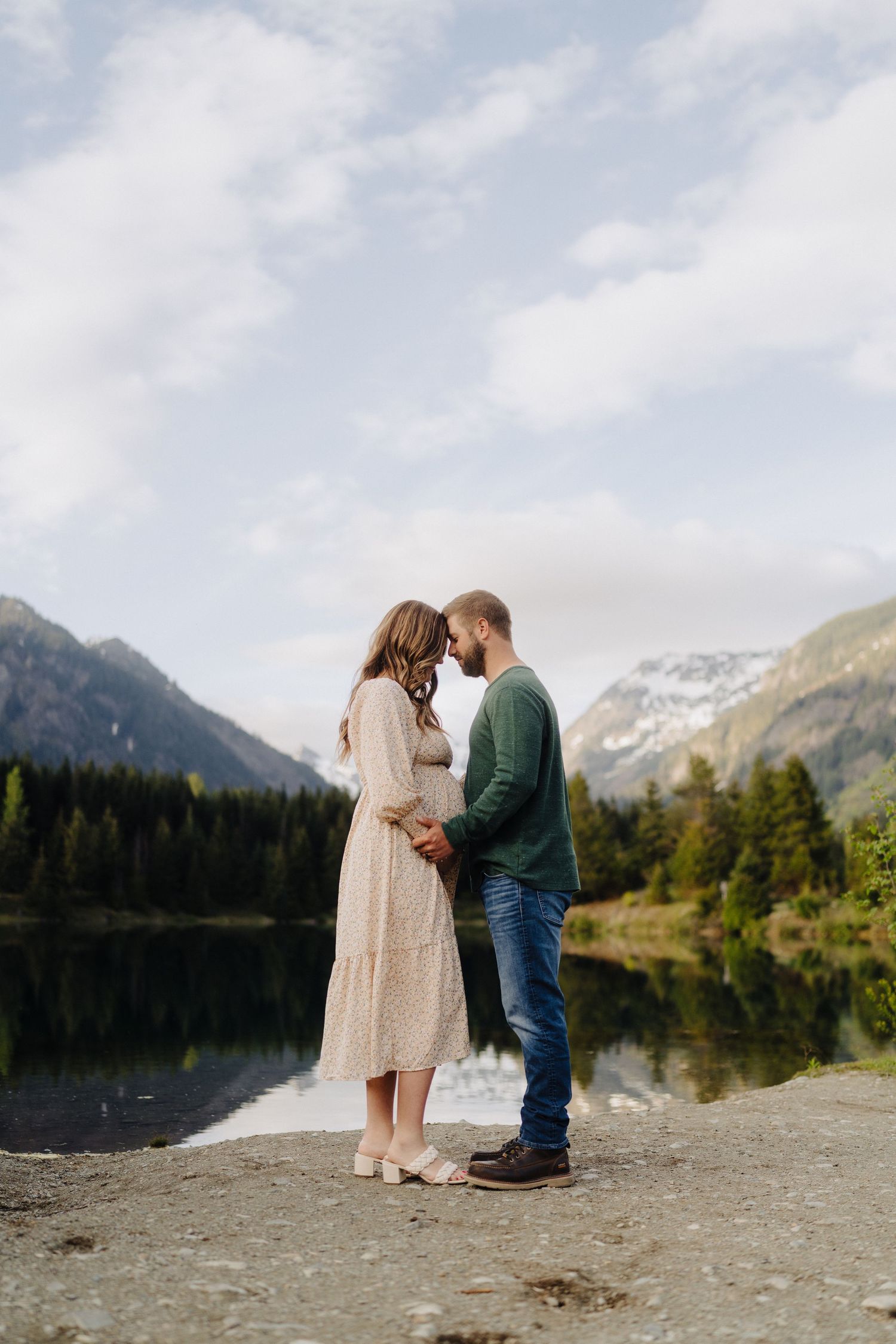 A tender moment between a couple on a lakeside beach with majestic mountains in the background.