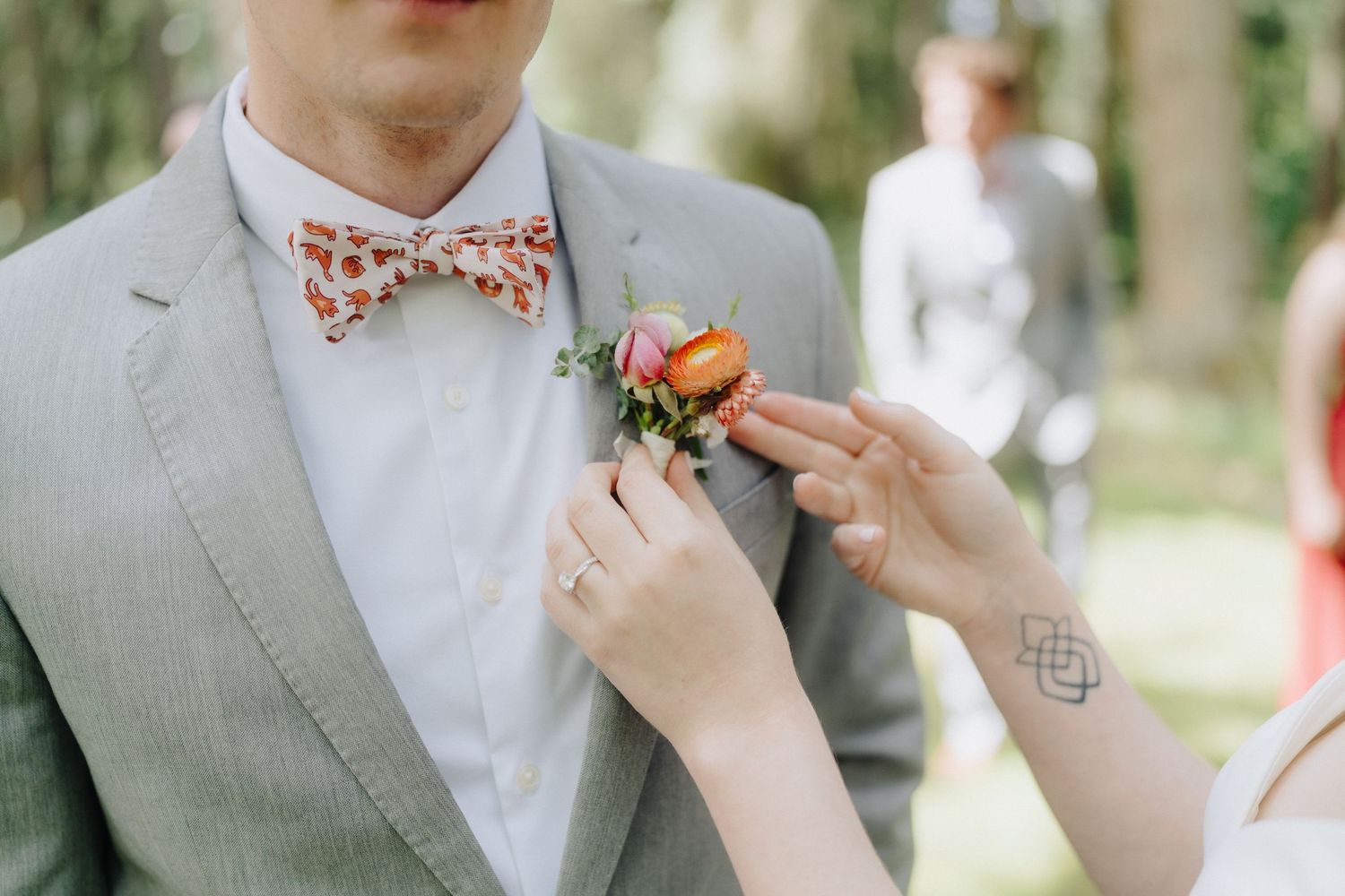 A close-up shot of a polka dot bowtie being adjusted on a light gray suit with a white boutonniere.