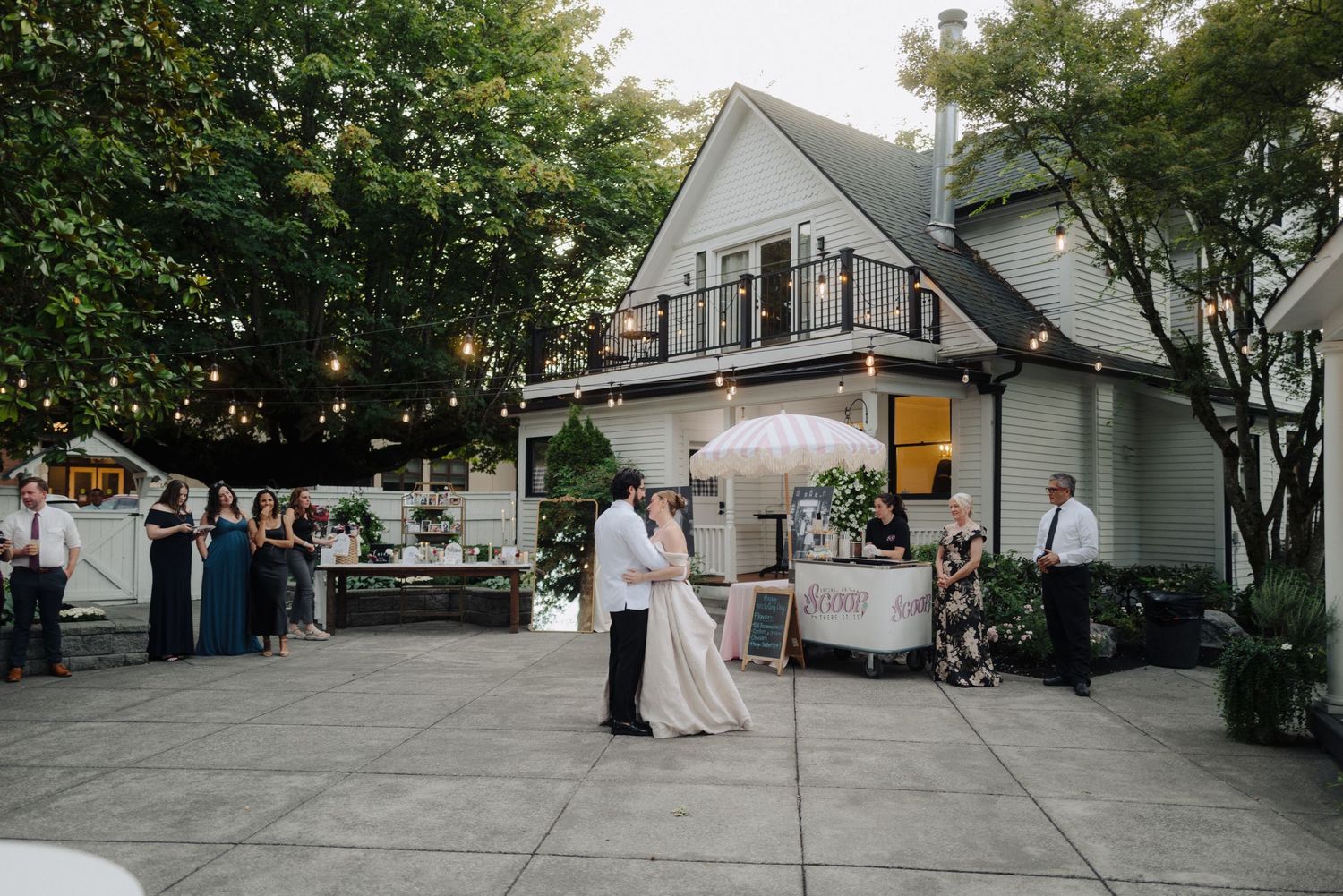 Evening wedding reception outside a white A-frame house with string lights and catering setup.