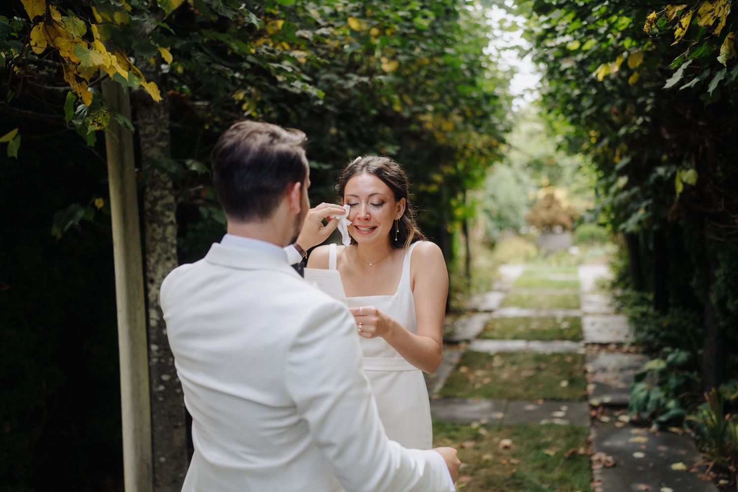 A couple shares a joyful moment together on a garden path lined with green foliage.
