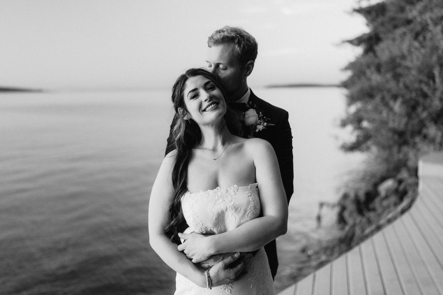 Couple shares an intimate moment during their wedding photoshoot on a scenic waterfront deck.