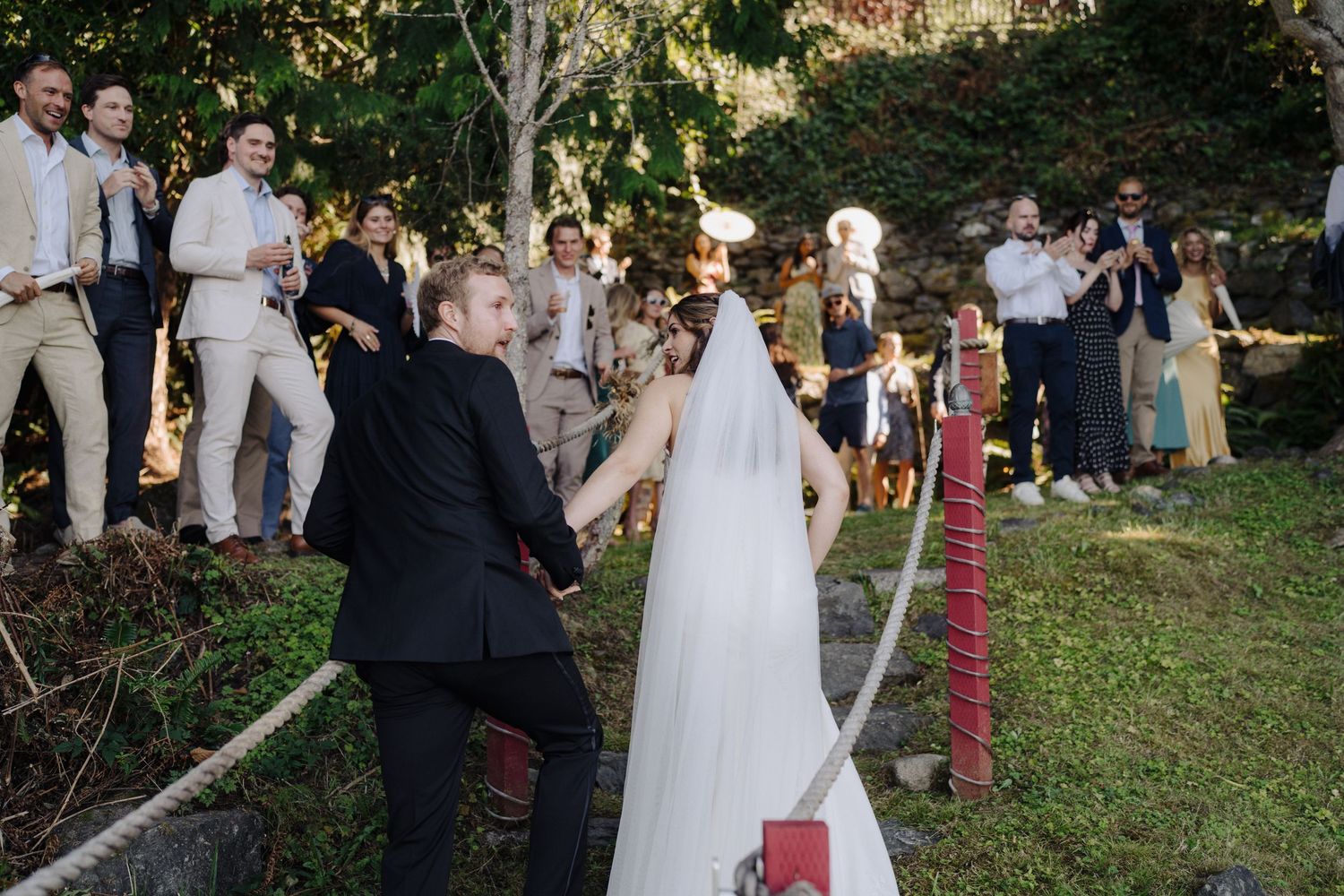 Wedding ceremony processional on a roped pathway with guests watching from both sides.
