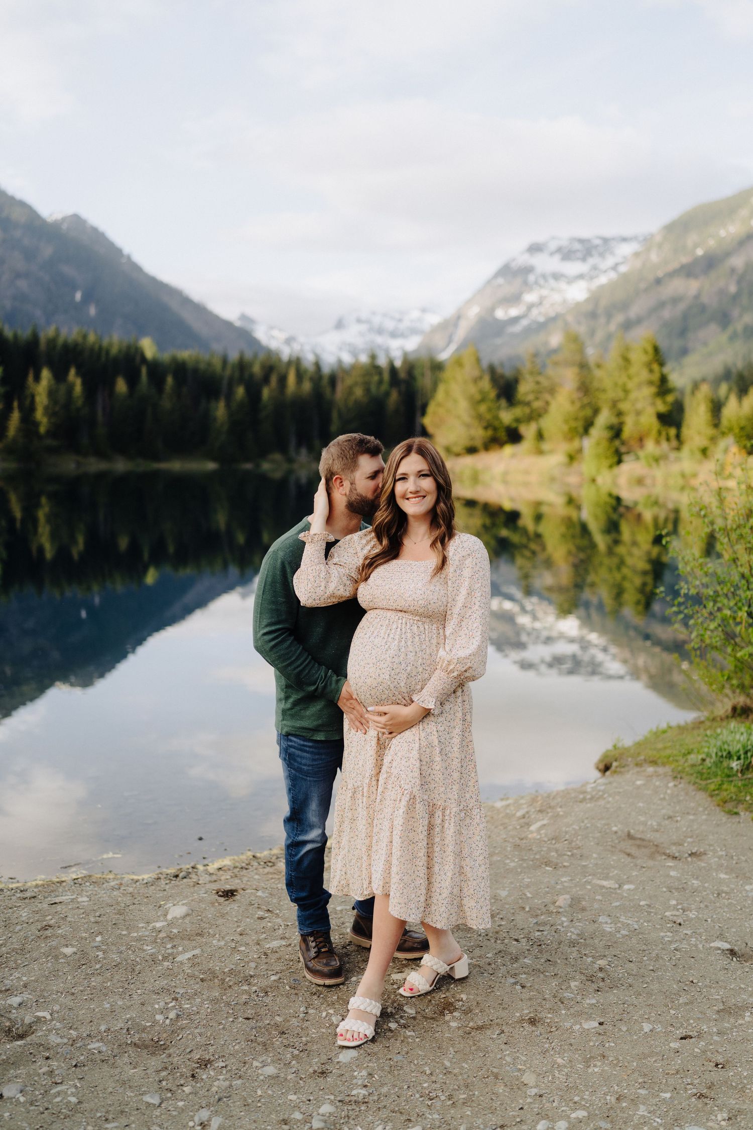 Sweet interaction between couple on shoreline with stunning mountain lake reflection in background.