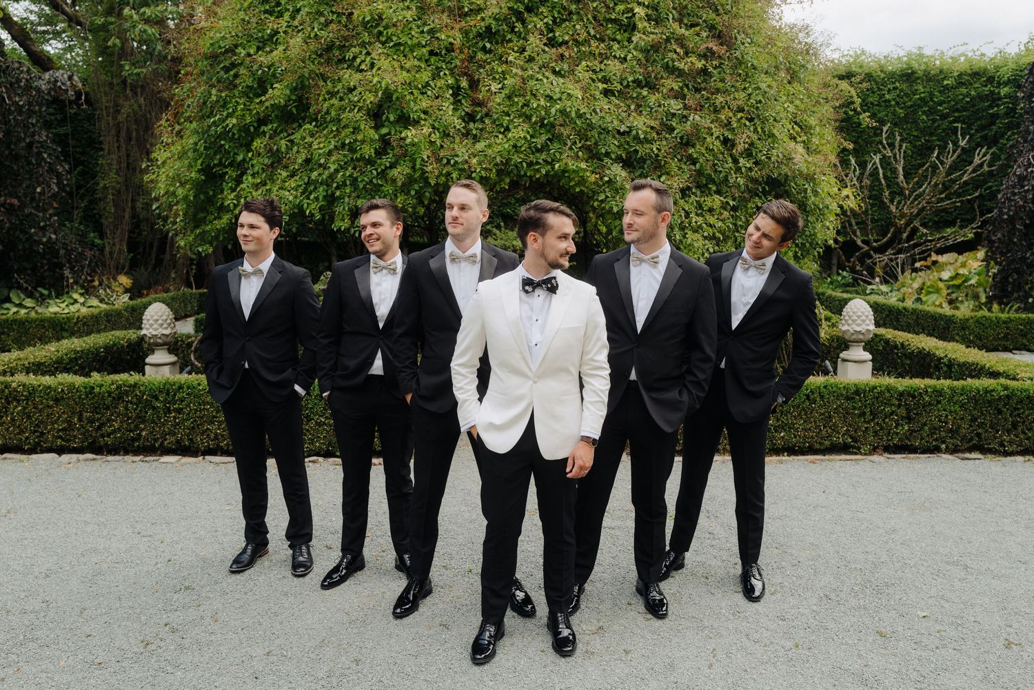 Groomsmen walking together in black suits and bowties on garden pathway.