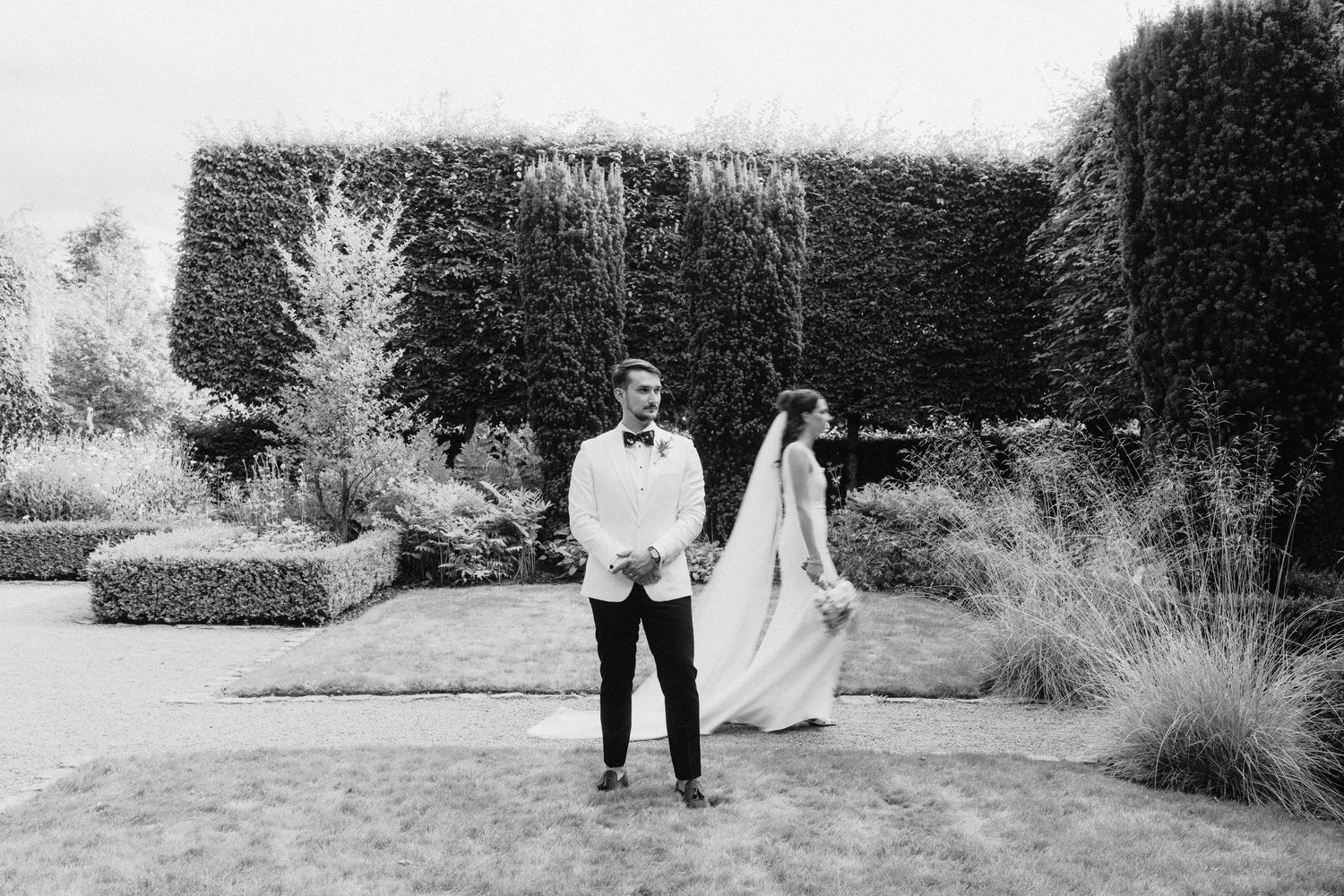 Black and white wedding photography of couple walking through garden landscape.
