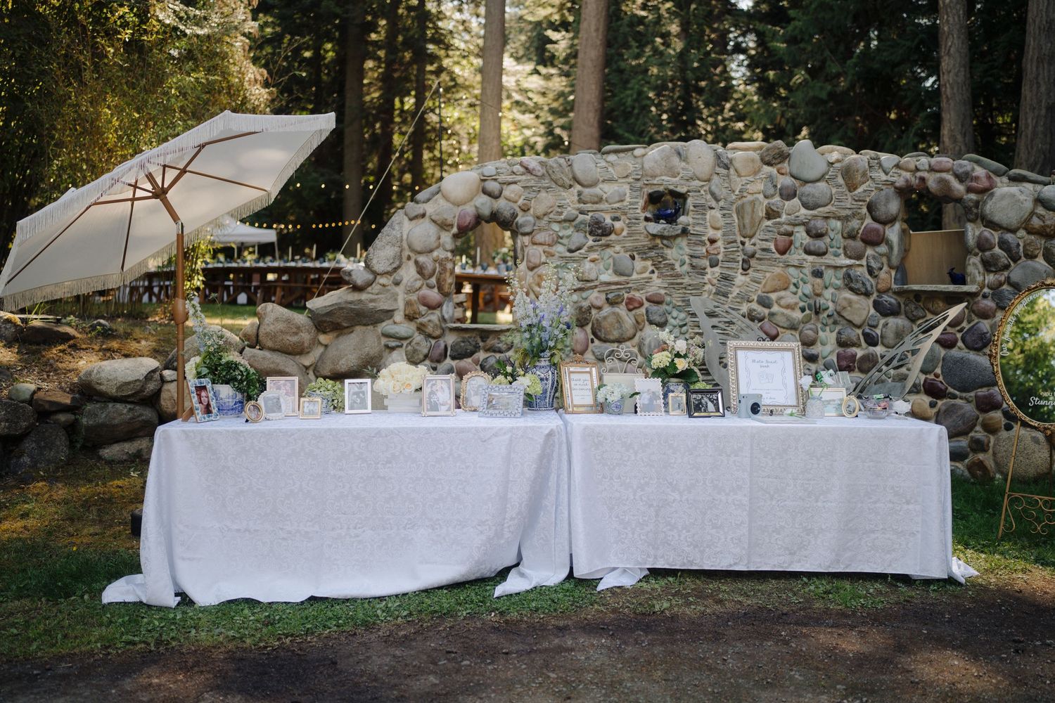 Long white reception tables set up against a rustic stone wall backdrop outdoors.
