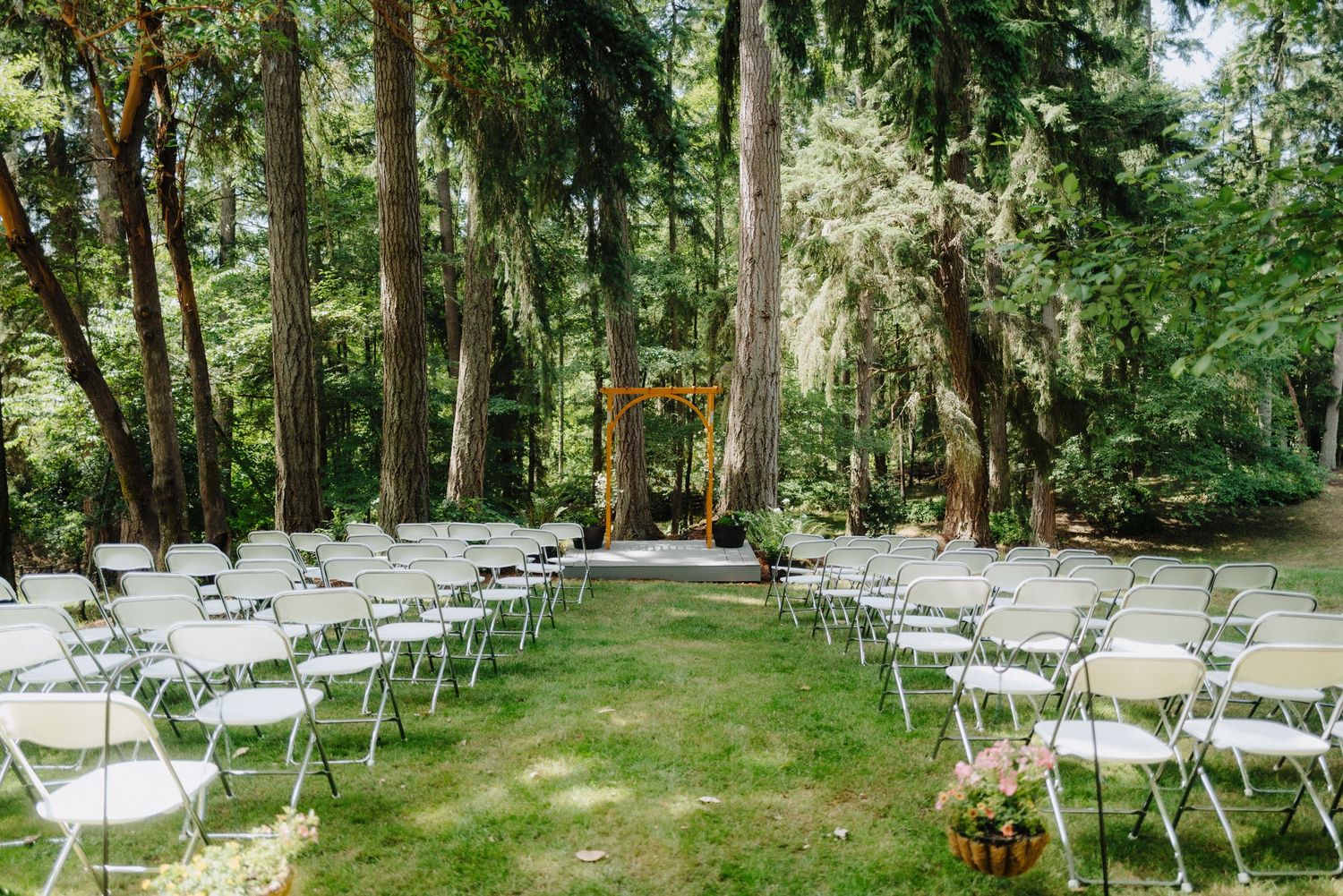 White folding chairs line a natural woodland aisle for an outdoor forest wedding ceremony.