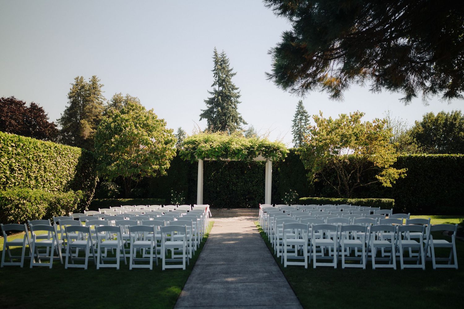 White chairs set up in rows for an outdoor garden wedding ceremony.