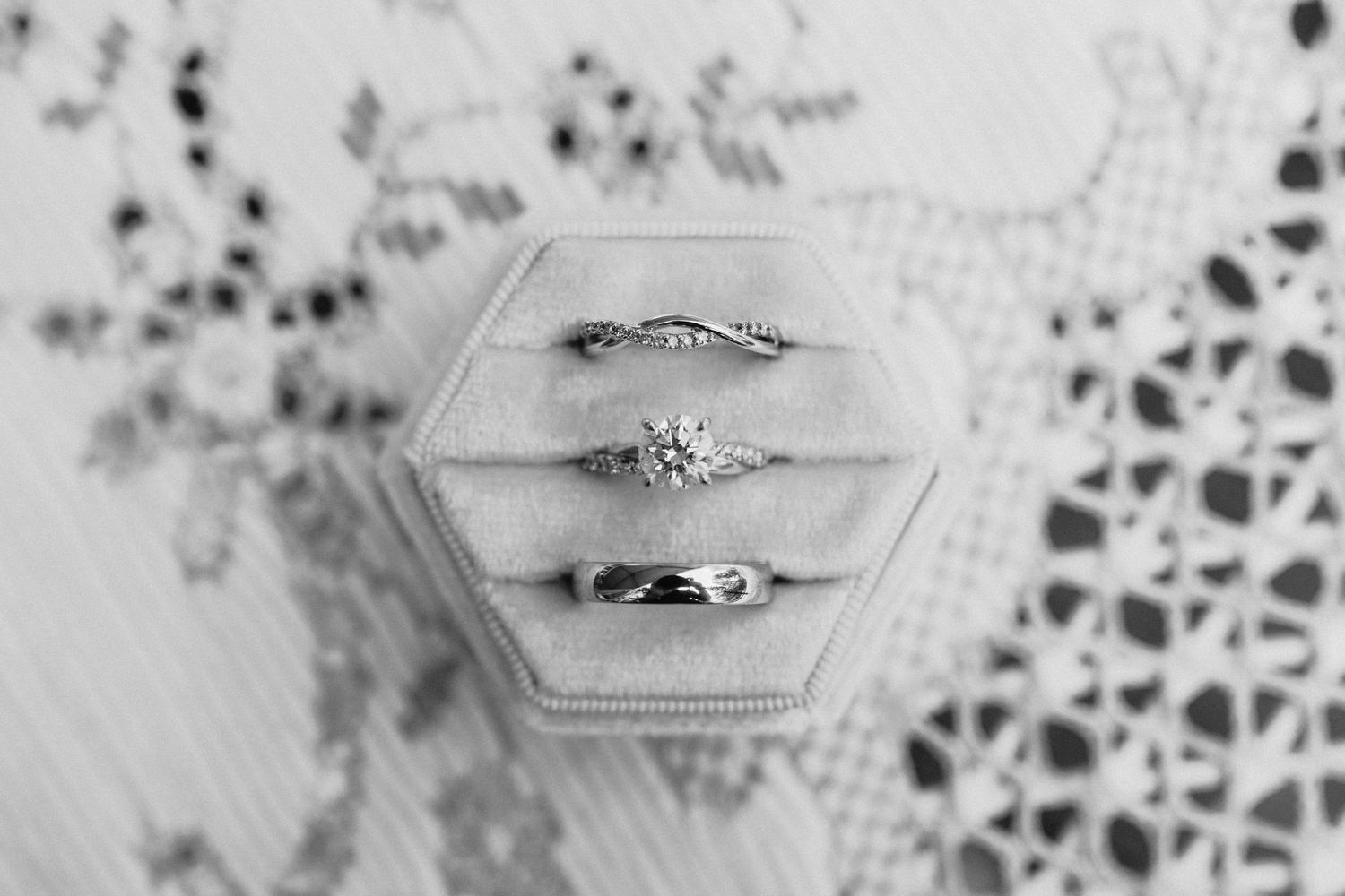 Three elegant wedding rings displayed in a hexagonal box against a delicate lace background.