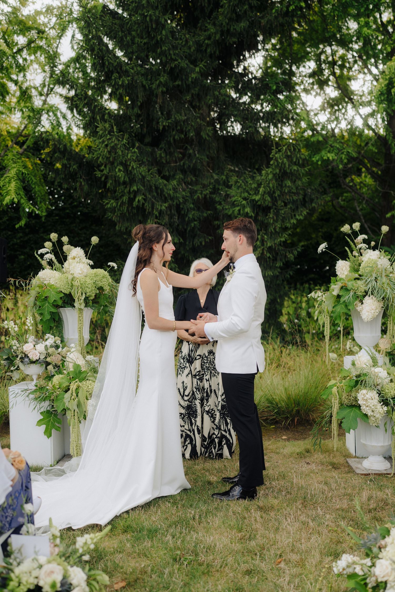 Wedding ceremony in progress with elegant white floral arrangements and decorative urns.