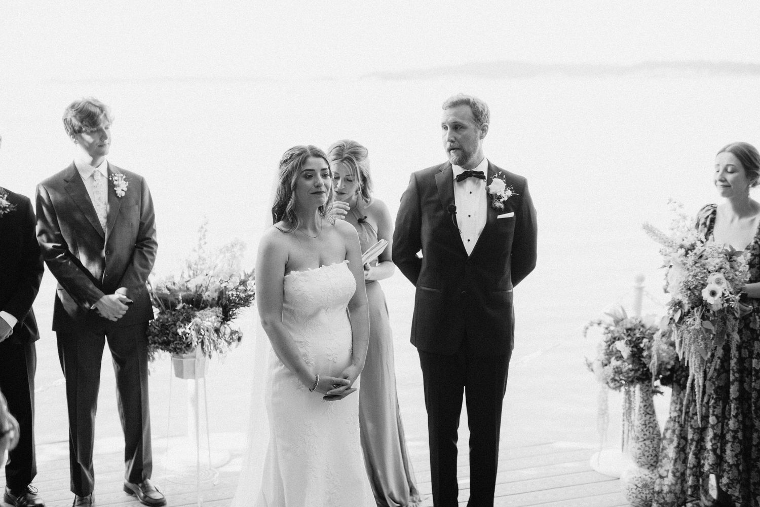 Wedding party members in formal attire pose together outdoors for black and white photo series.