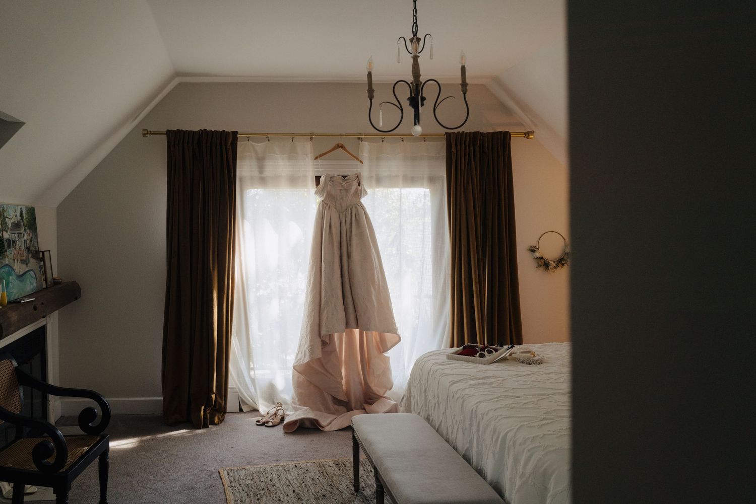 A dark bedroom interior with a chandelier and white curtains filtering natural light through the windows.