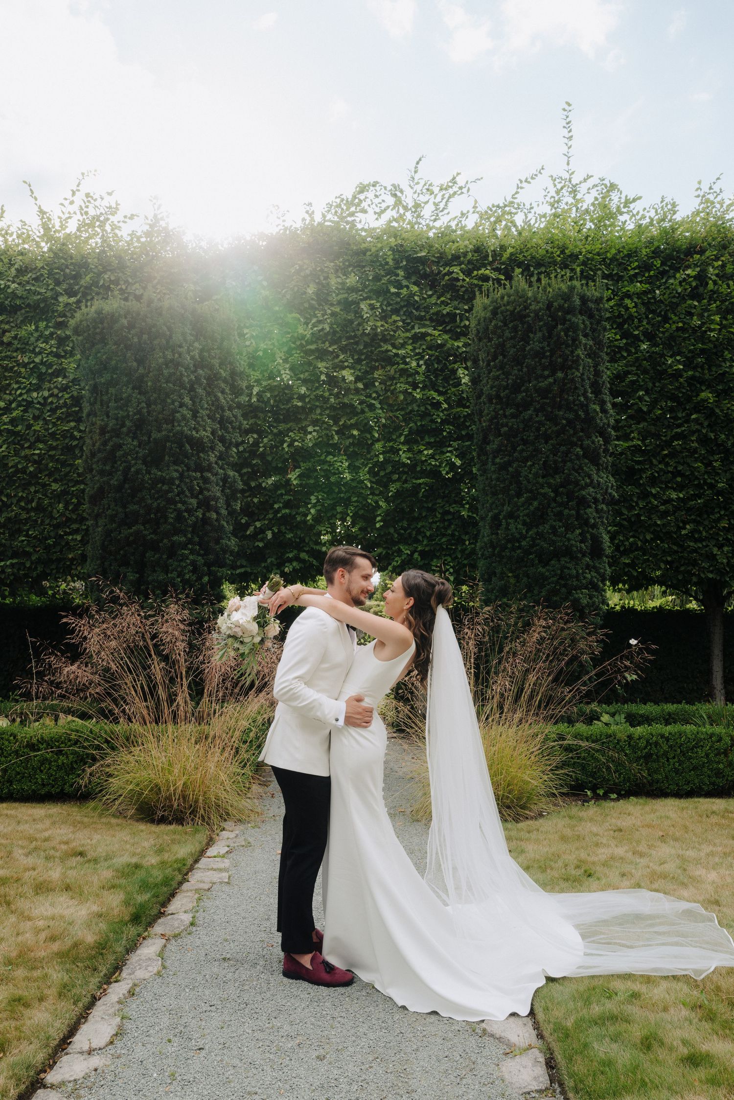 Newlyweds share intimate moments in a garden setting with flowing white dress and veil.