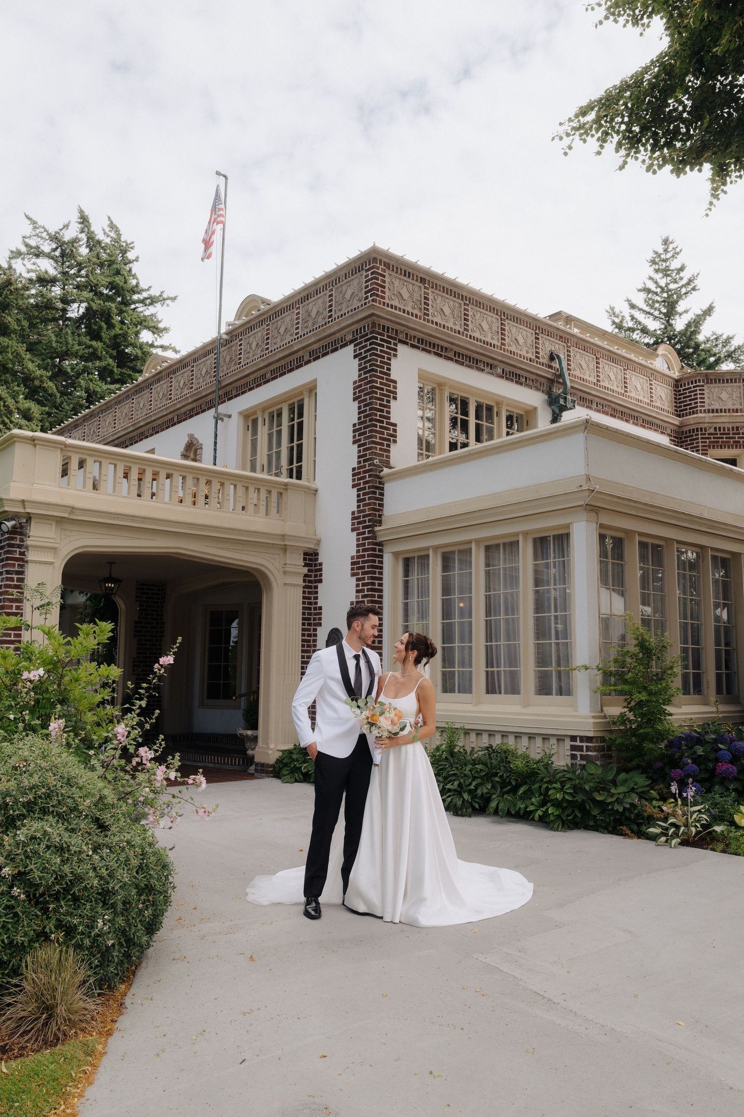 Wedding portrait in front of a grand historic building with American flag and beautiful landscaping.