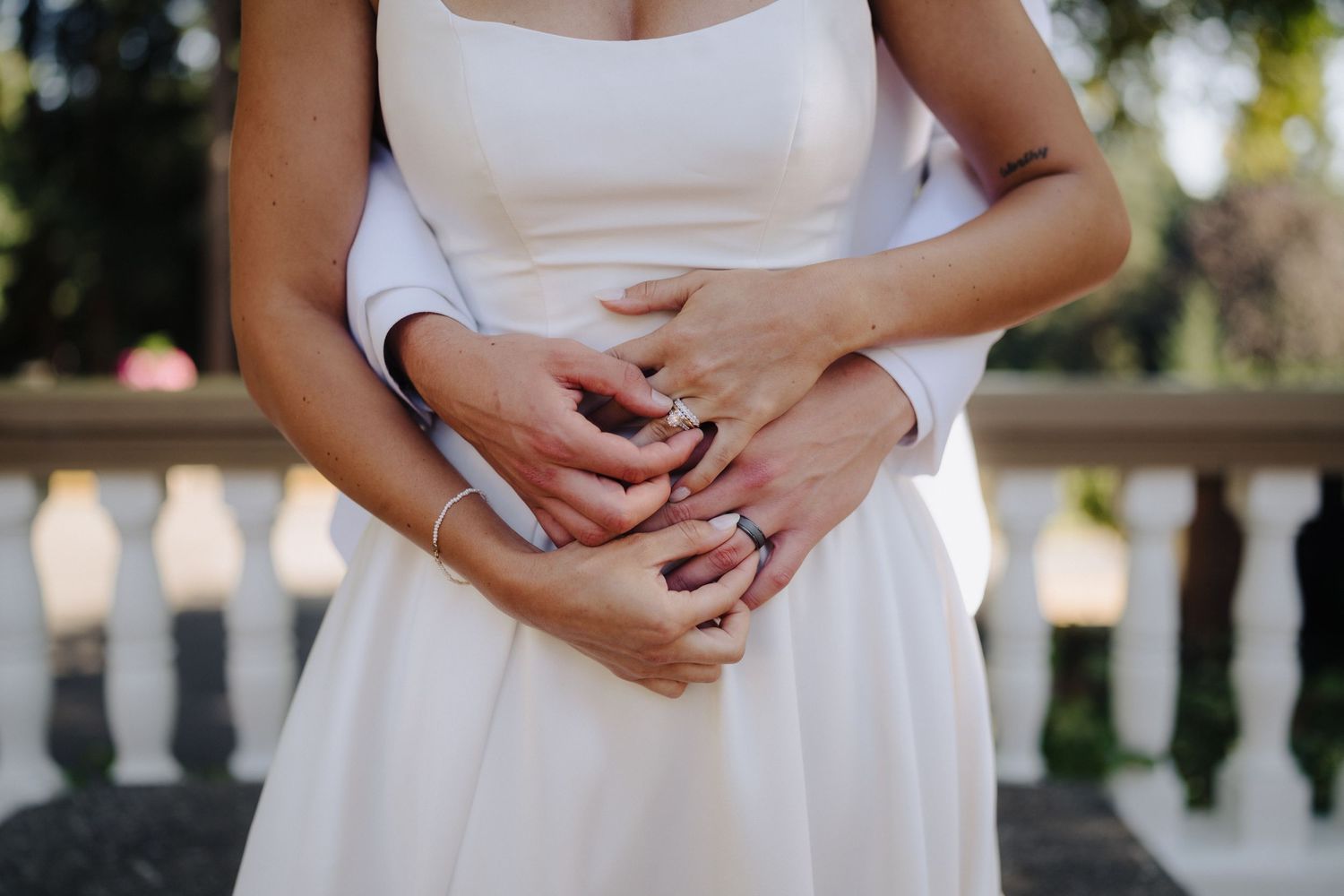 Close-up detail of hands resting on a white wedding dress against a balustrade.