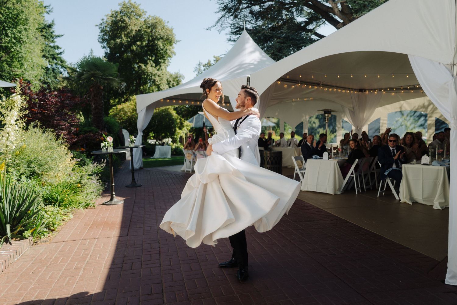 Wedding celebration under white tent with guests and dancing on brick patio.