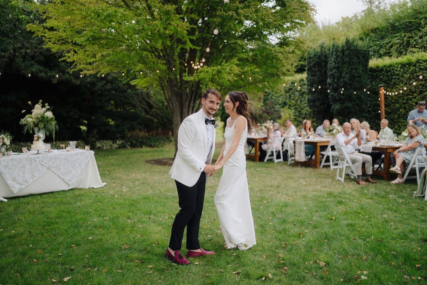 Garden wedding celebration with guests gathered under green trees.