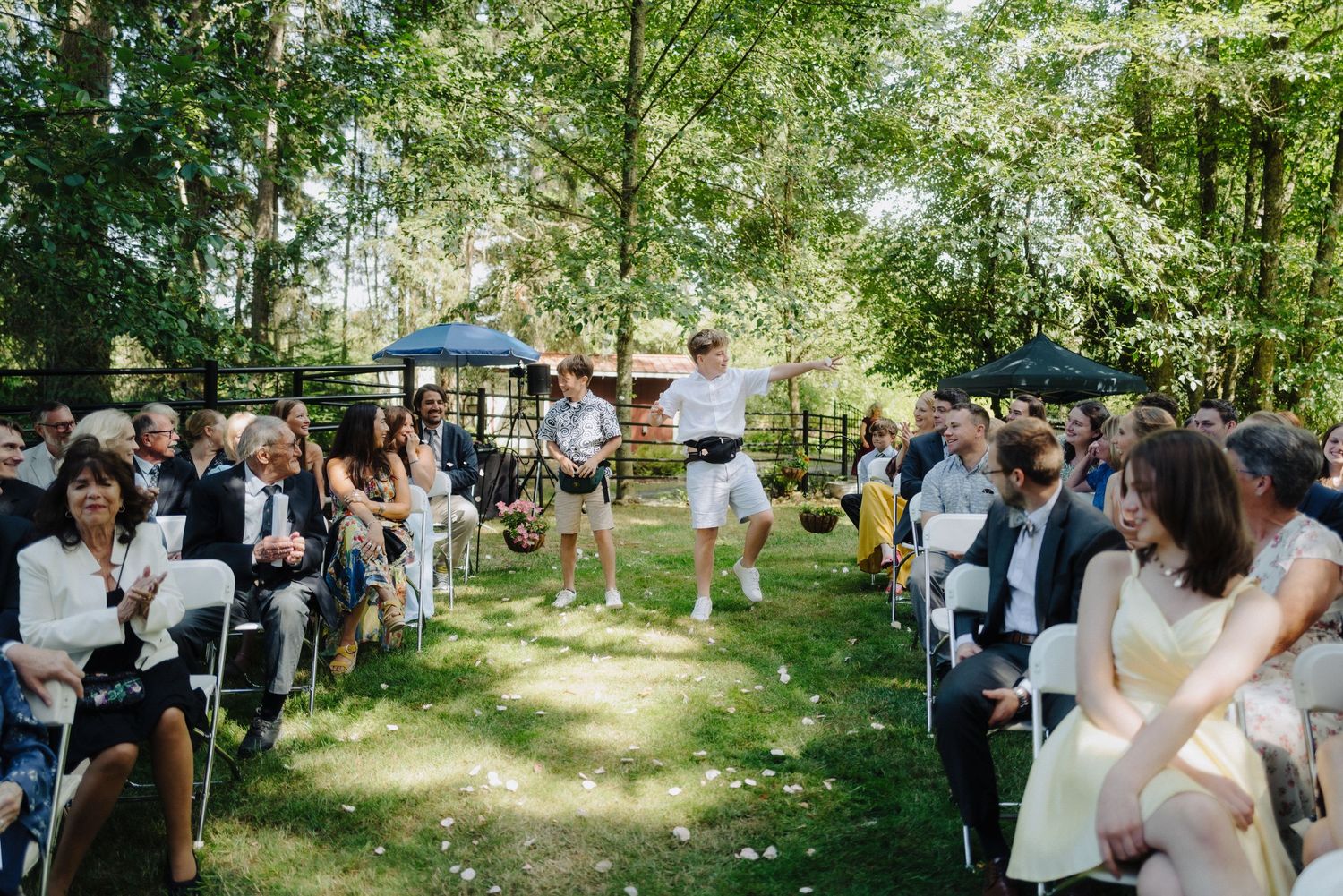 Wedding guests seated in white chairs during an outdoor forest ceremony.