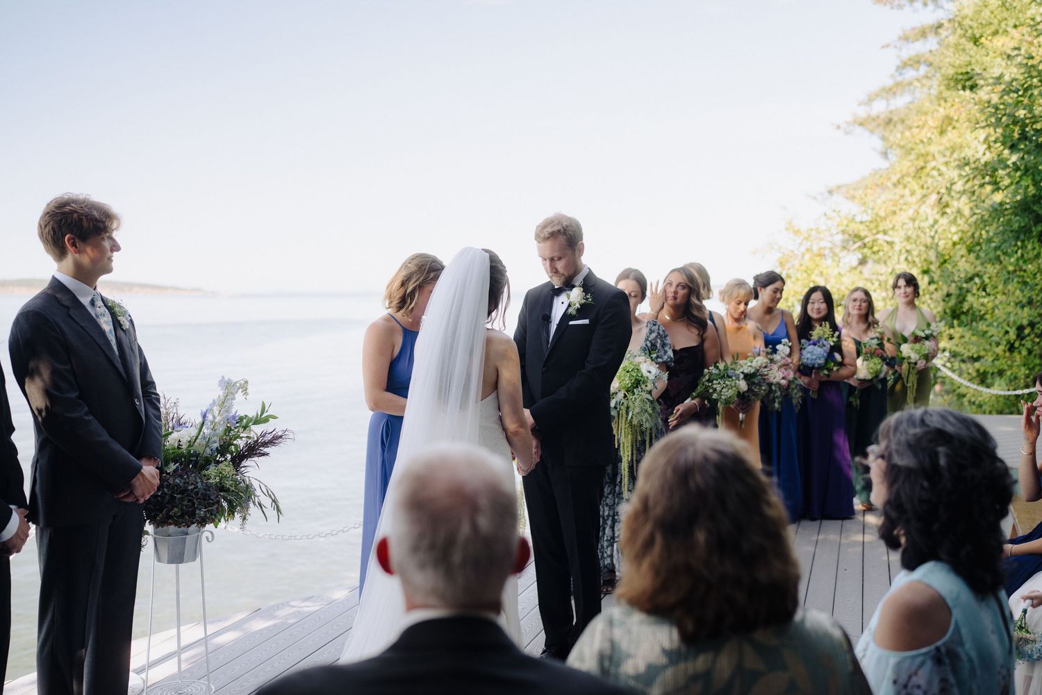 Waterfront wedding ceremony with guests gathered on deck overlooking scenic ocean view.