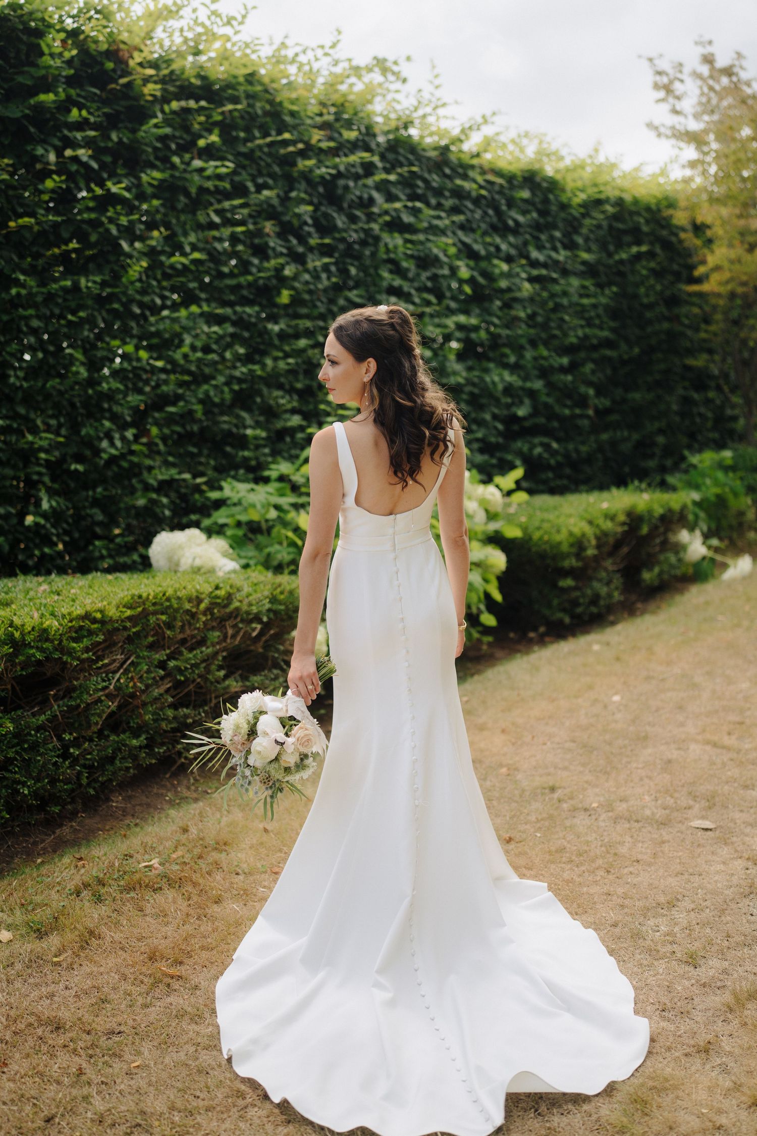 A bride in a flowing white dress twirls in a garden setting with greenery in the background.