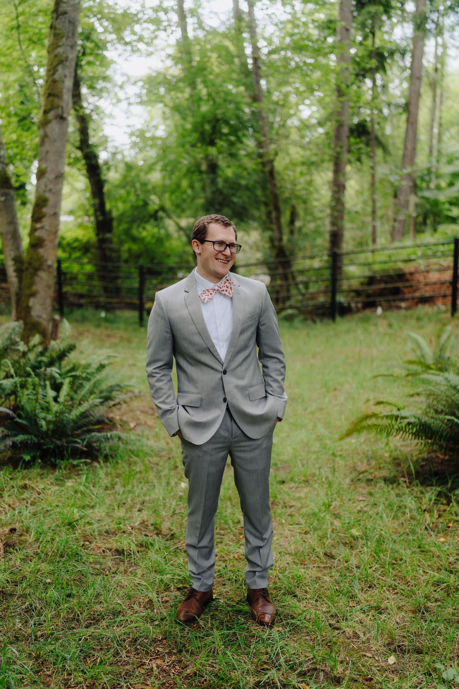 Groom in gray suit poses for portraits in a serene forest setting.